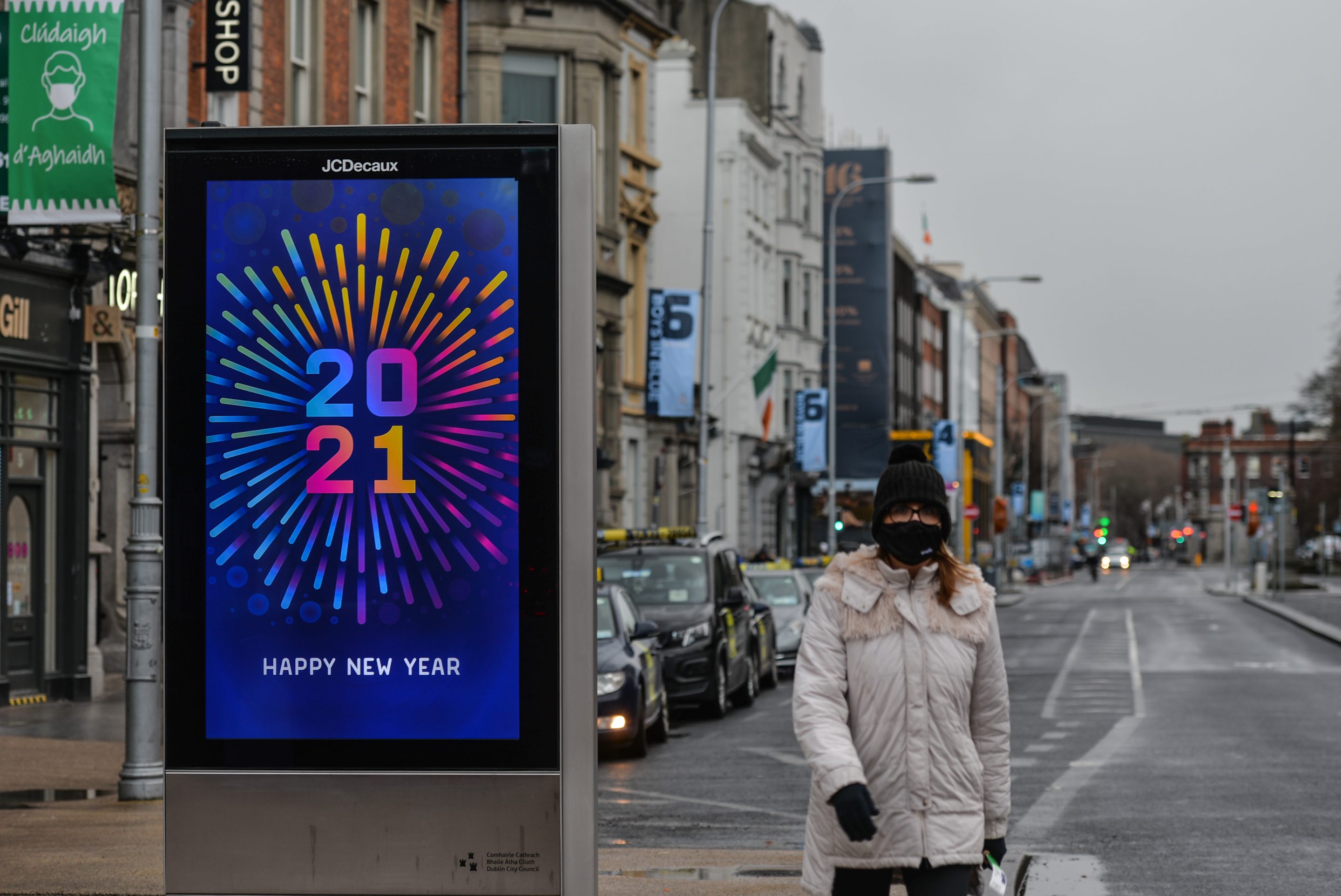A woman wearing a face mask passes by a street billboard 'Happy New Year 2021' seen in Dublin city center.