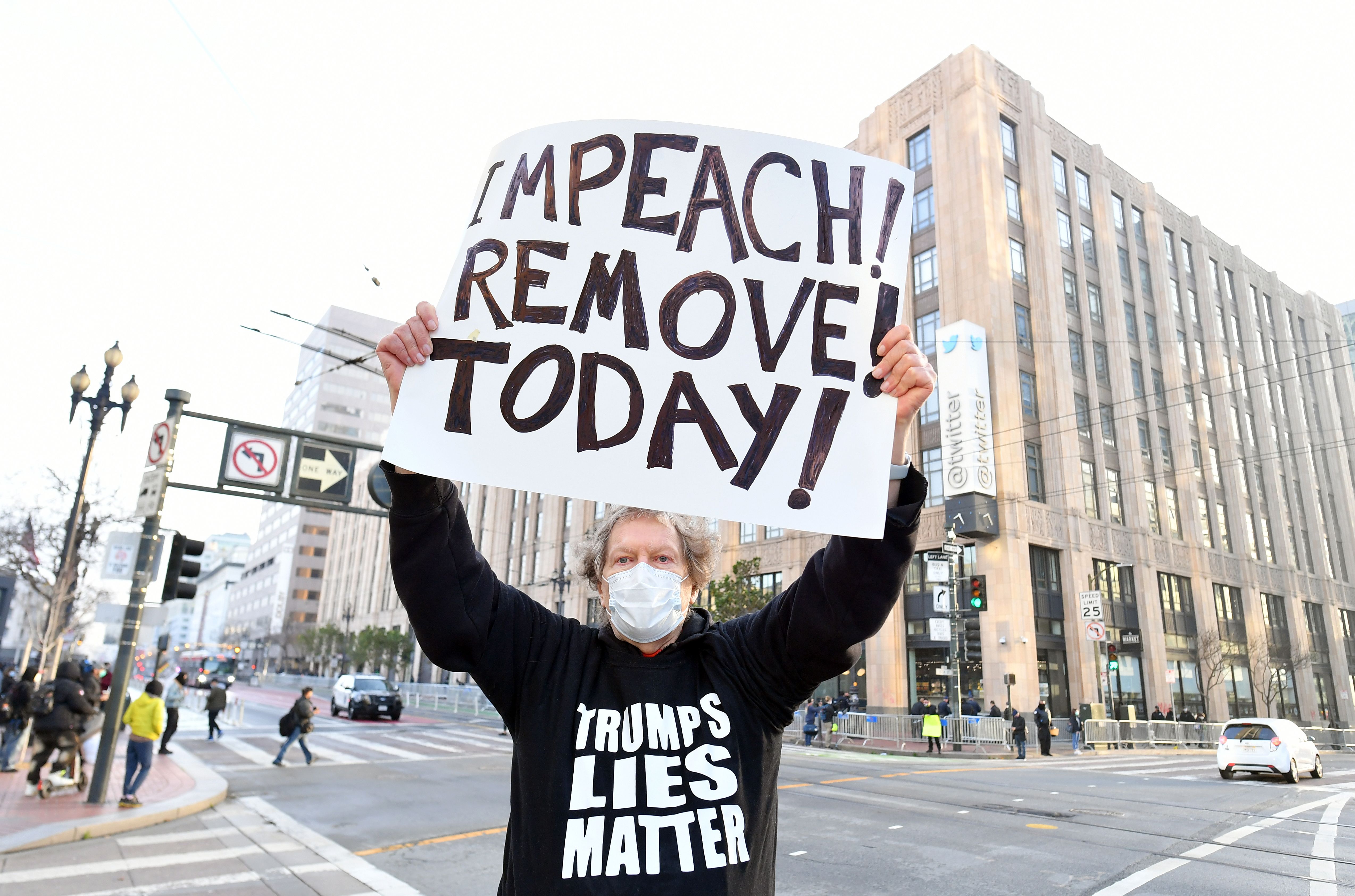 Protester Kenneth Lundgreen holds up a sign calling for the impeachment of President Donald Trump as police put together barricades outside Twitter corporate headquarters in San Francisco, California on January 11, 2021.