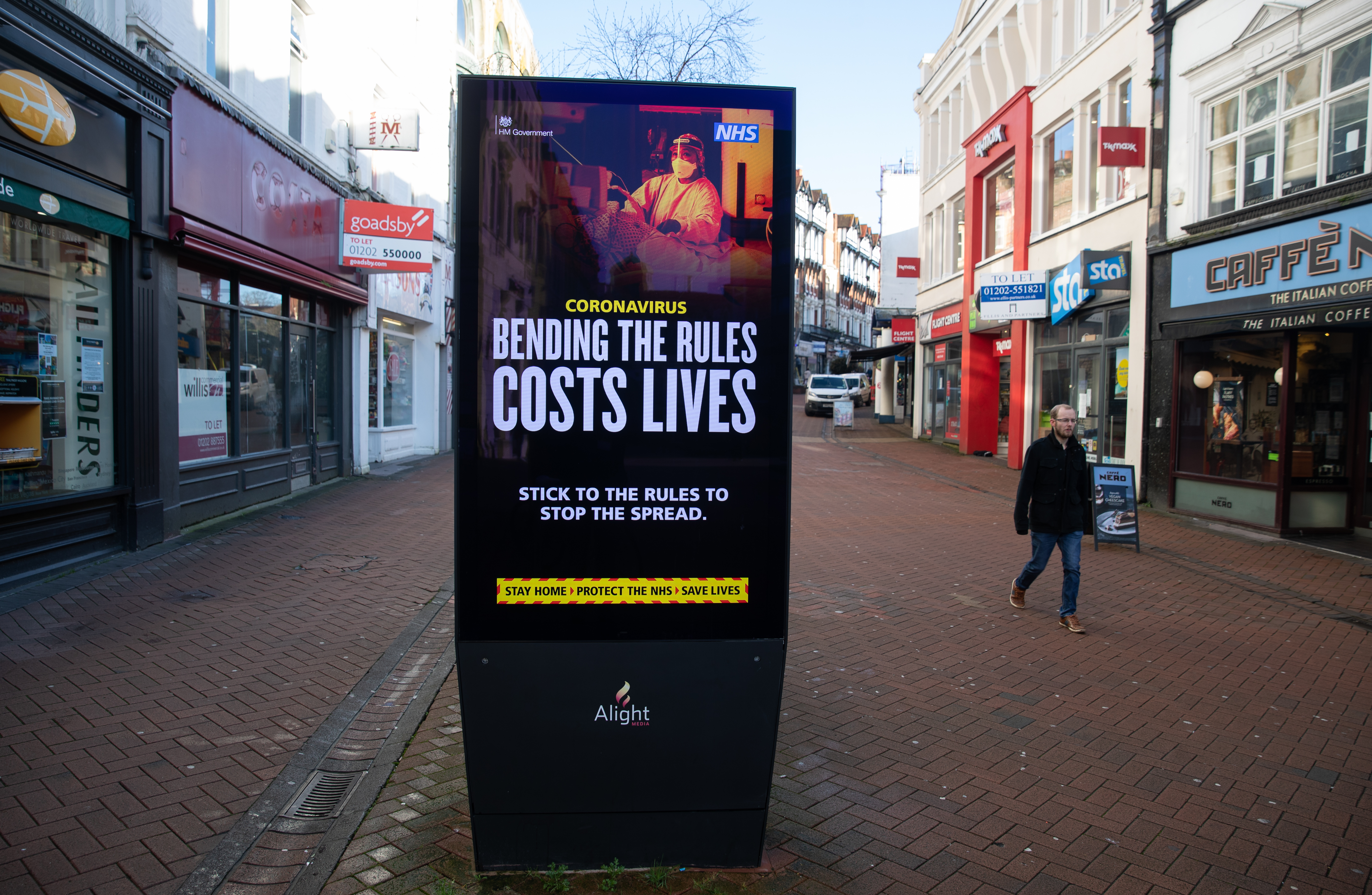 A person passes a 'Bending the rules costs lives' government coronavirus sign on Old Christchurch road in Bournemouth, during England's third national lockdown to curb the spread of coronavirus.