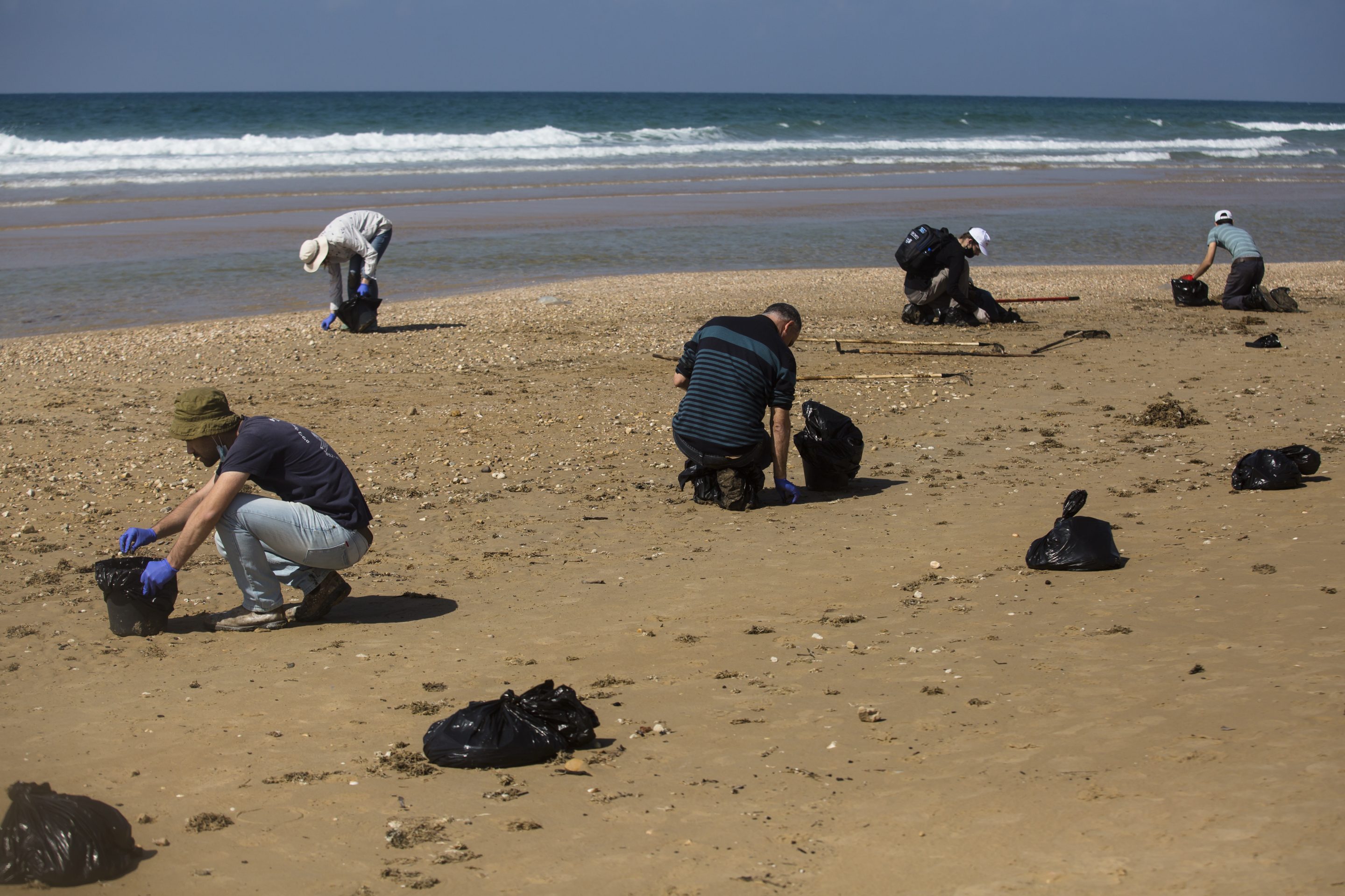 People cleaning tar off a beach in Israel after an oil spill.