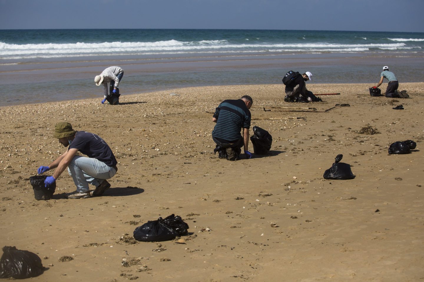 People cleaning tar off a beach in Israel after an oil spill.