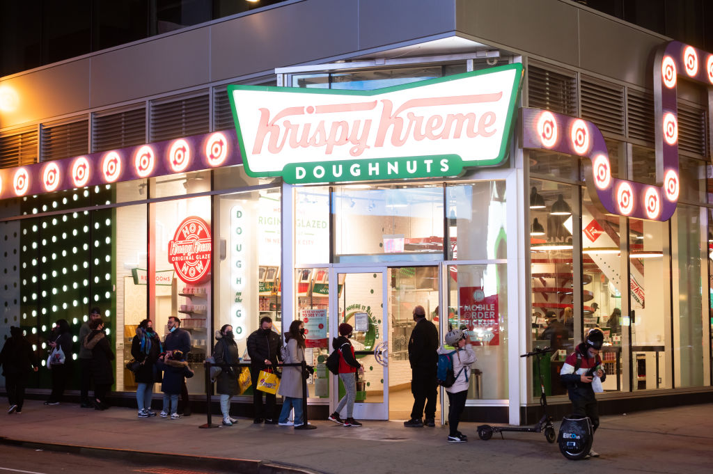 People line up outside Krispy Kreme in Times Square amid the coronavirus pandemic on March 17, 2021, in New York City. After undergoing various shutdown orders for the past 12 months, the city is currently in phase 4 of its reopening plan, allowing for the reopening of low-risk outdoor activities, movie and television productions, and indoor dining, as well as the opening of movie theaters, all with capacity restrictions.