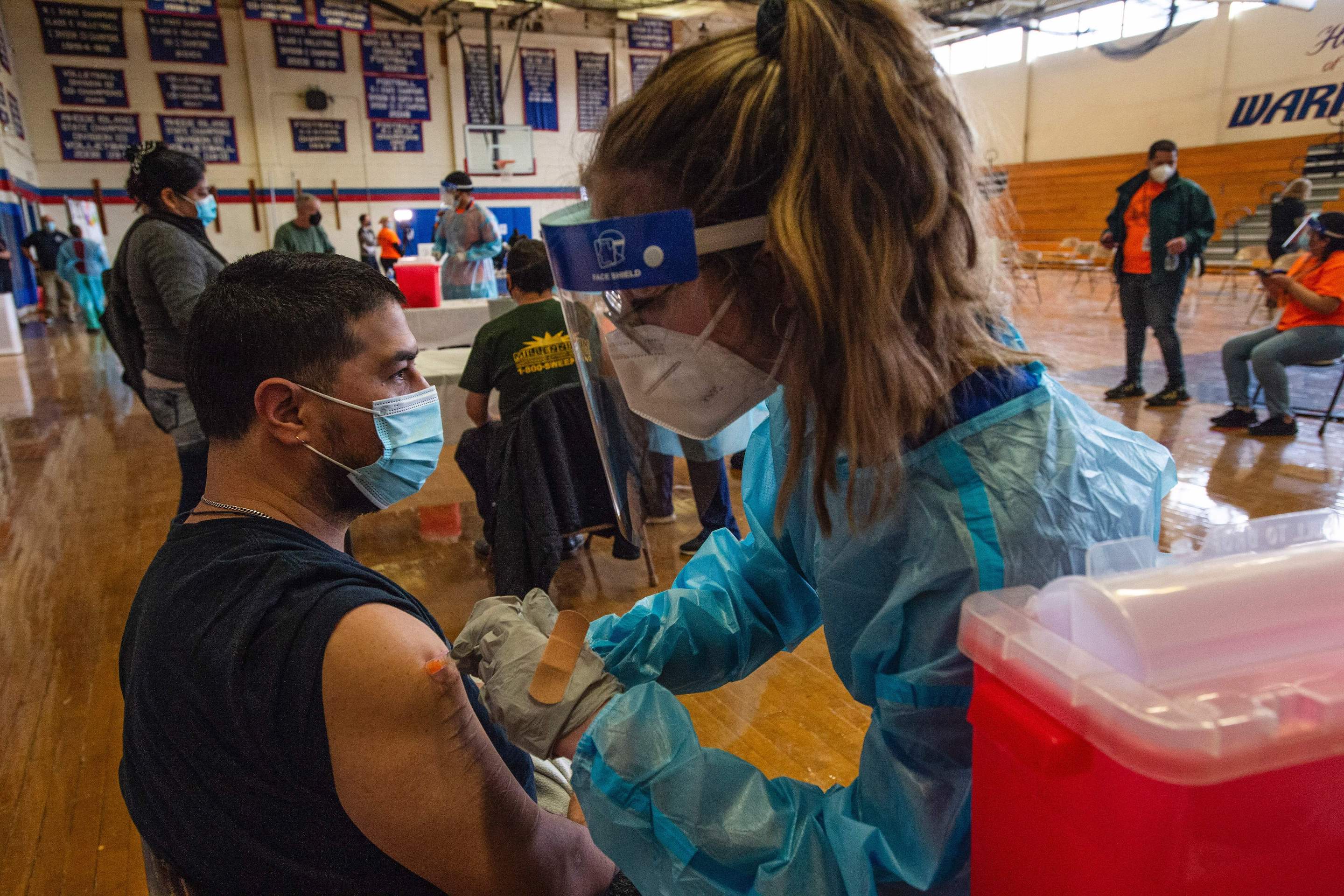 Alejandro Uribe, 43, is inoculated by pharmacy student Nicole Famiglietti at Central Falls High School in Central Falls, R.I., on Feb. 13, 2021. According to the U.S. Census Bureau, Central Falls is made up of over 66% Hispanic and almost 13% Black residents.