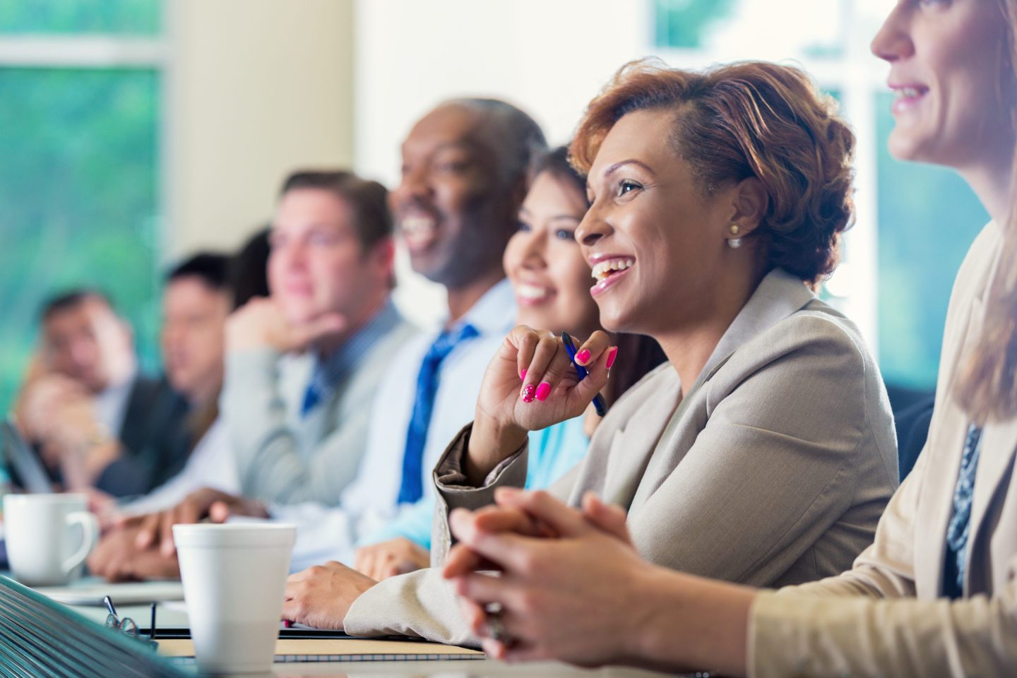 Woman attends business seminar, sitting at long table among other leaders.