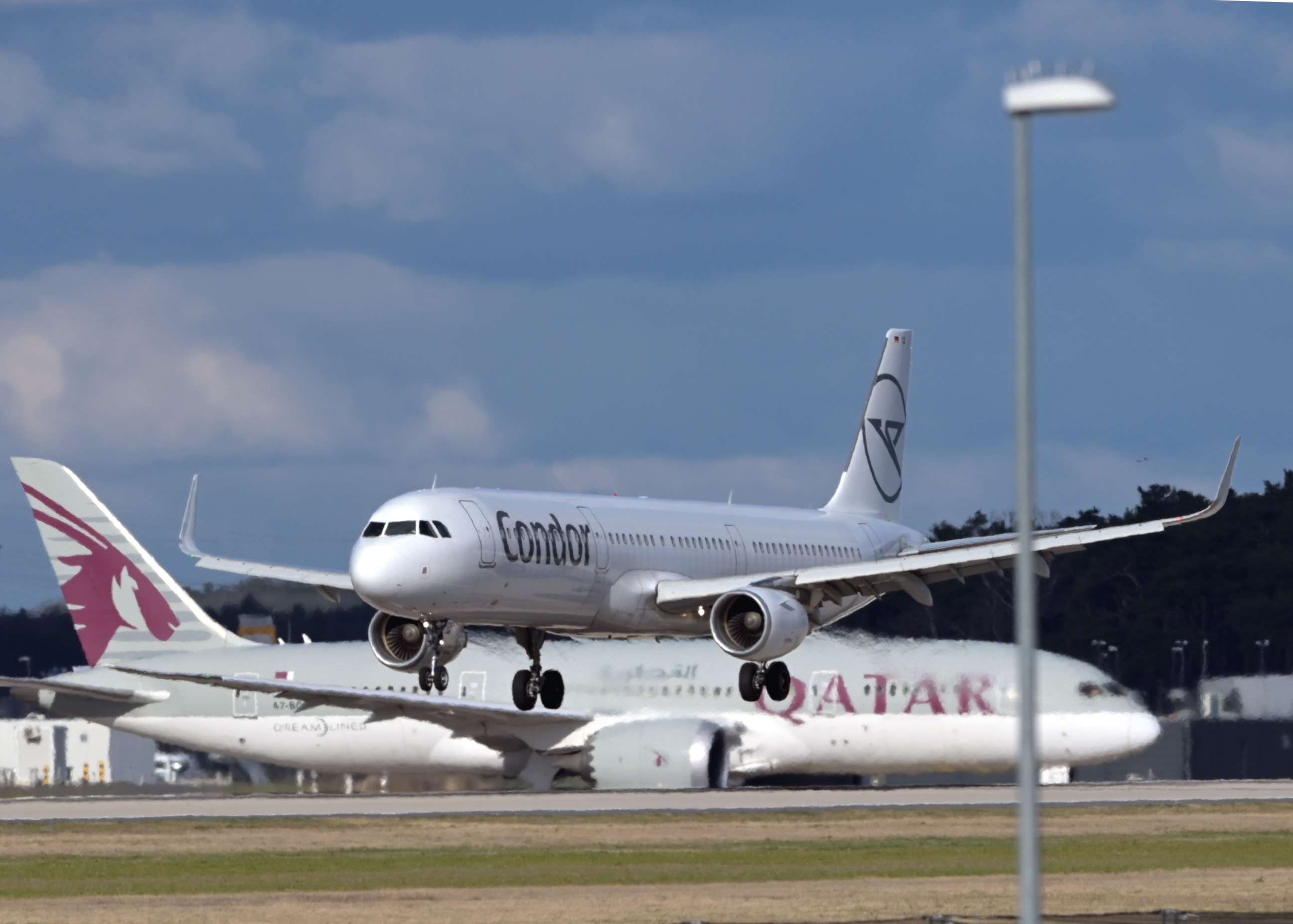 An Airbus A321 of the airline Condor landing while a Boeing 787 Dreamliner awaits takeoff clearance at Berlin Brandenburg Airport.