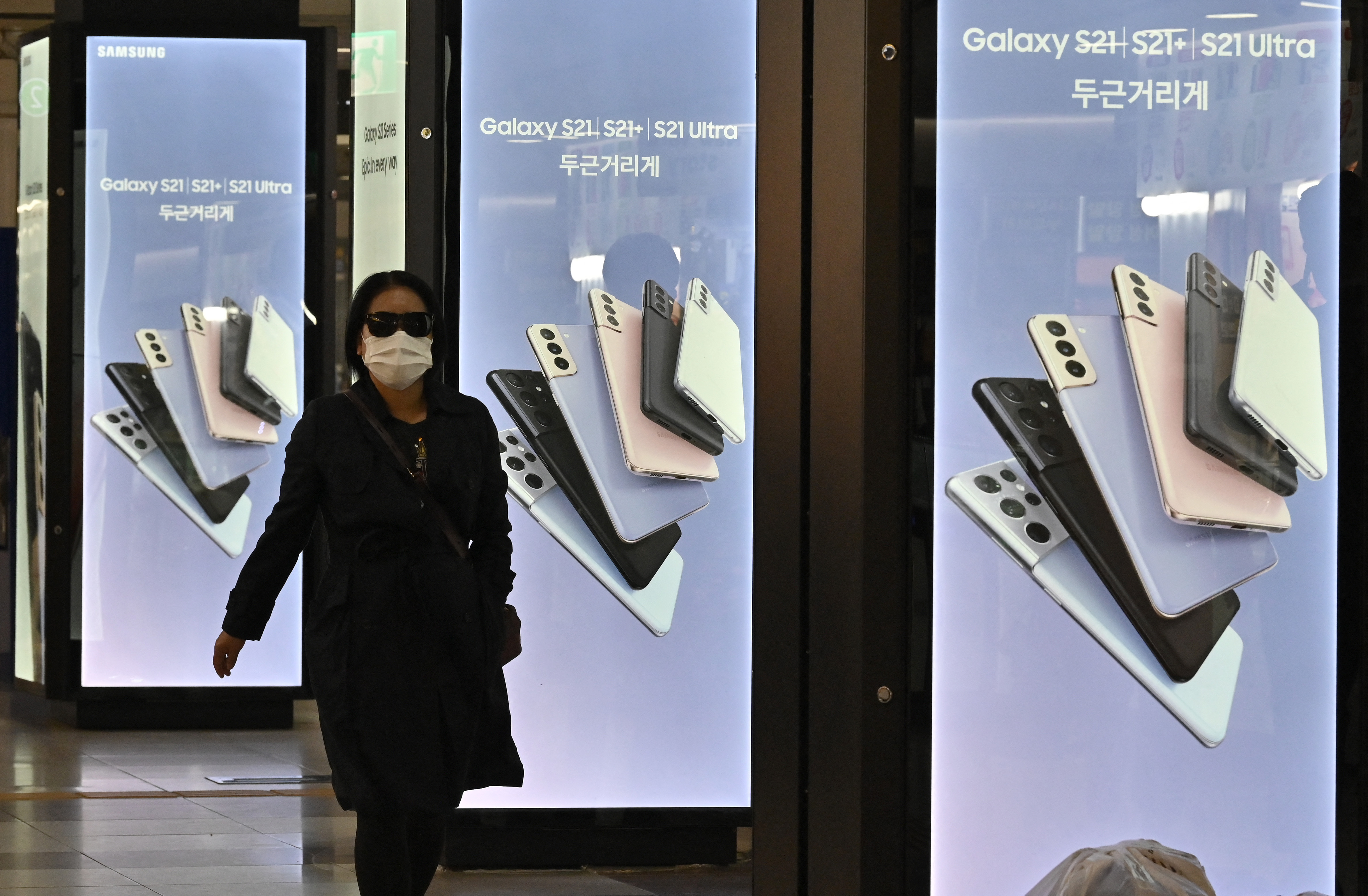 This picture taken on April 28, 2021 shows a woman walking past an advertisement for the Samsung Galaxy S21 smartphone at an underground shopping area in Seoul.