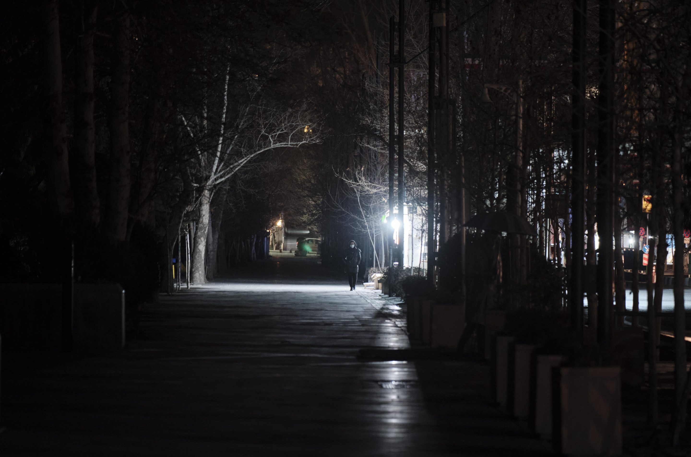 An Iranian woman wearing a protective face mask walks along a street-side during a power outage in northern Tehran at night on January 21, 2020.