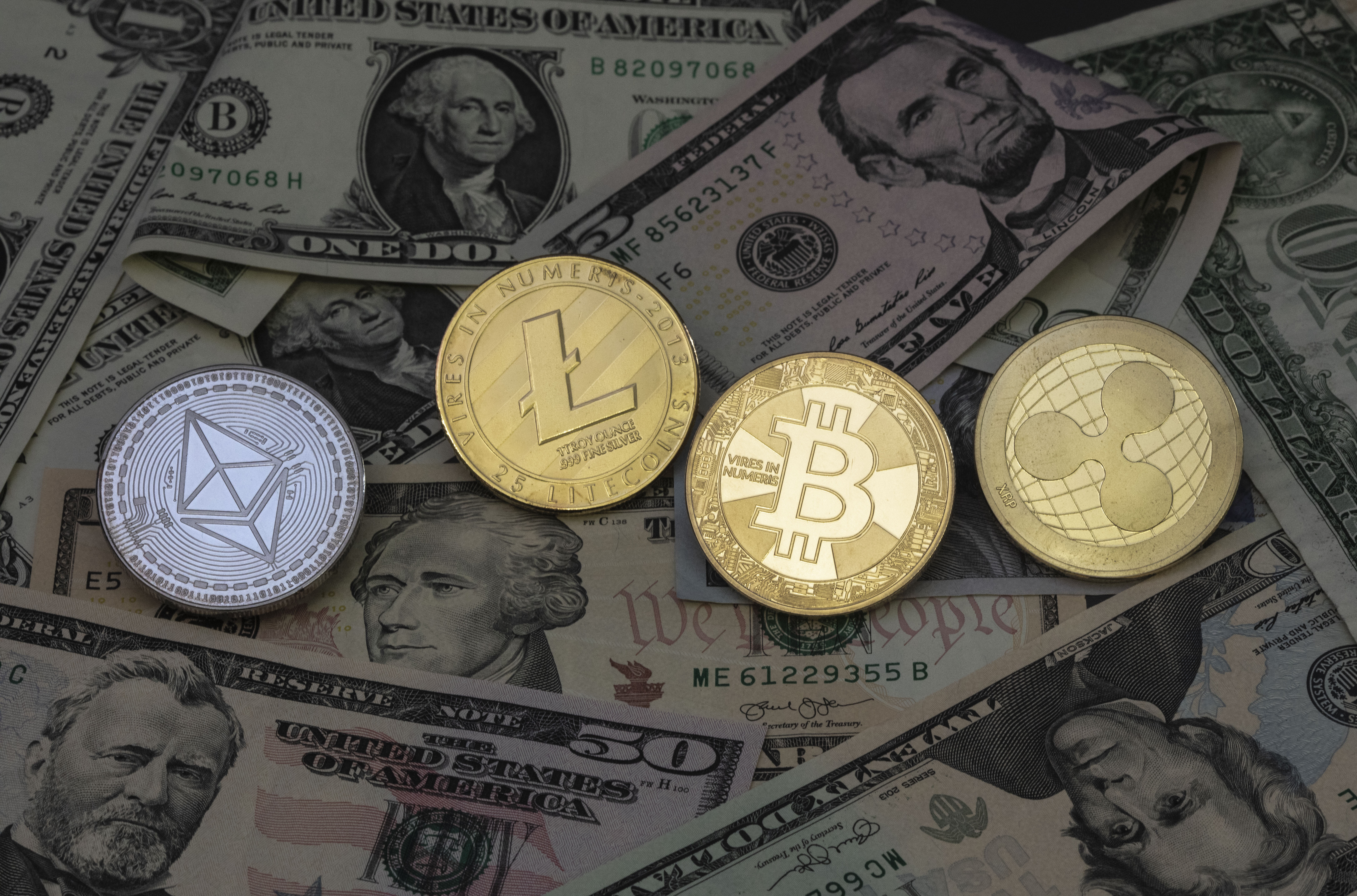 This illustration photo shows various dollar banknotes and physical Bitcoin, Ripple, Litecoin and Ethereum coins.