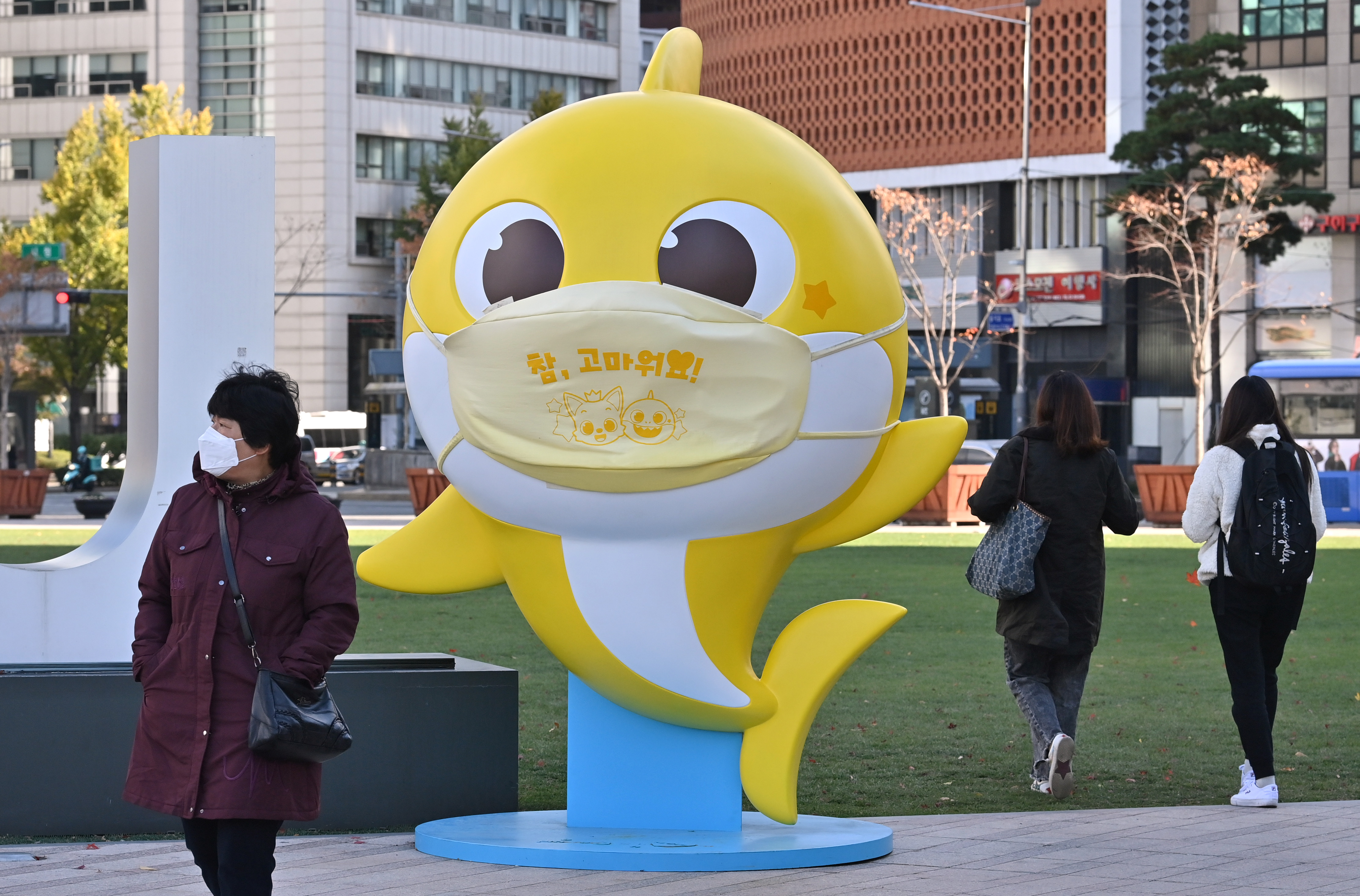 People walk past a shark character from the children's song "Baby Shark" at Seoul Plaza in Seoul on November 3, 2020