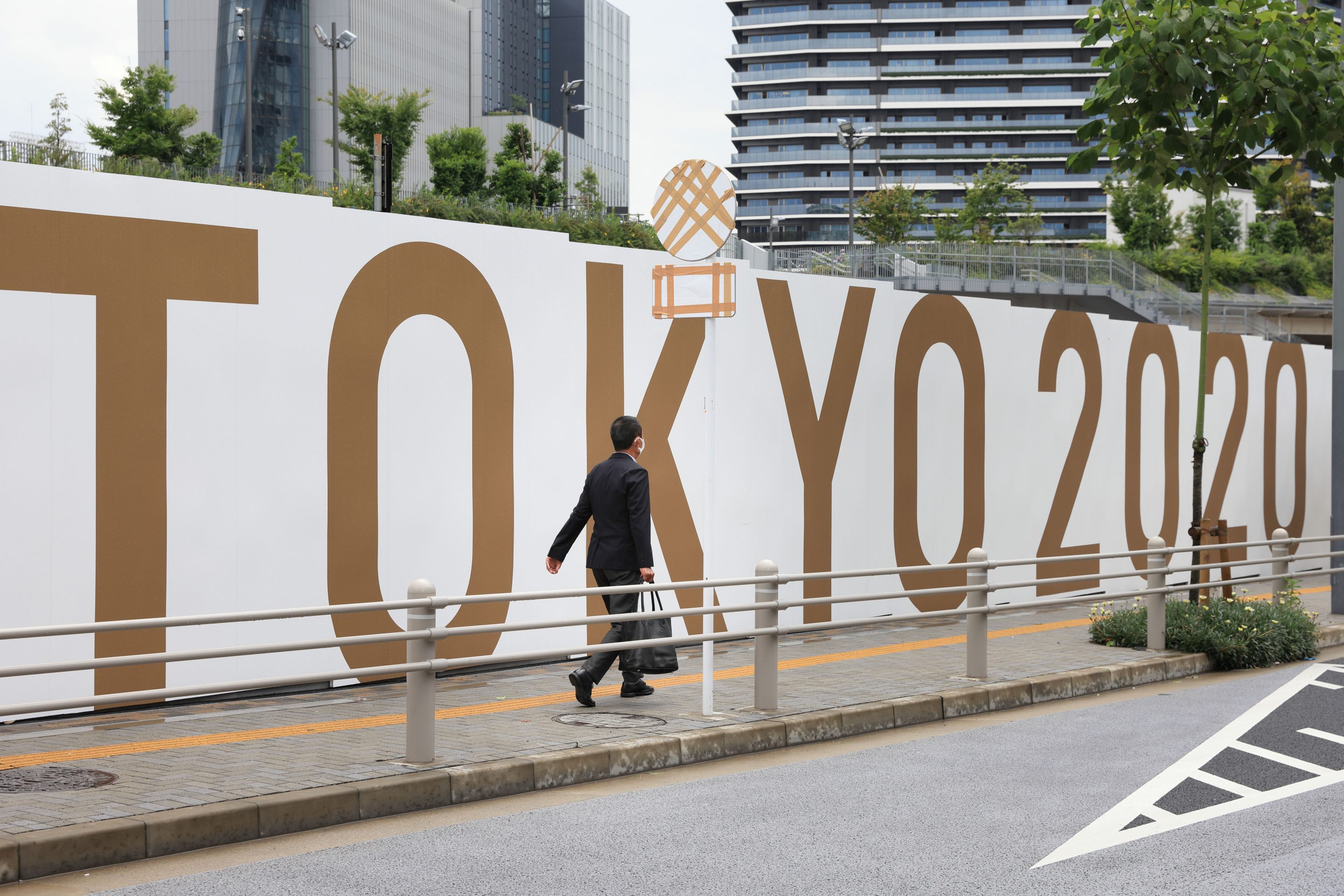 A businessman with a suitcase walks by Tokyo 2020 Olympic Games branding on the walls of the National Stadium construction site.