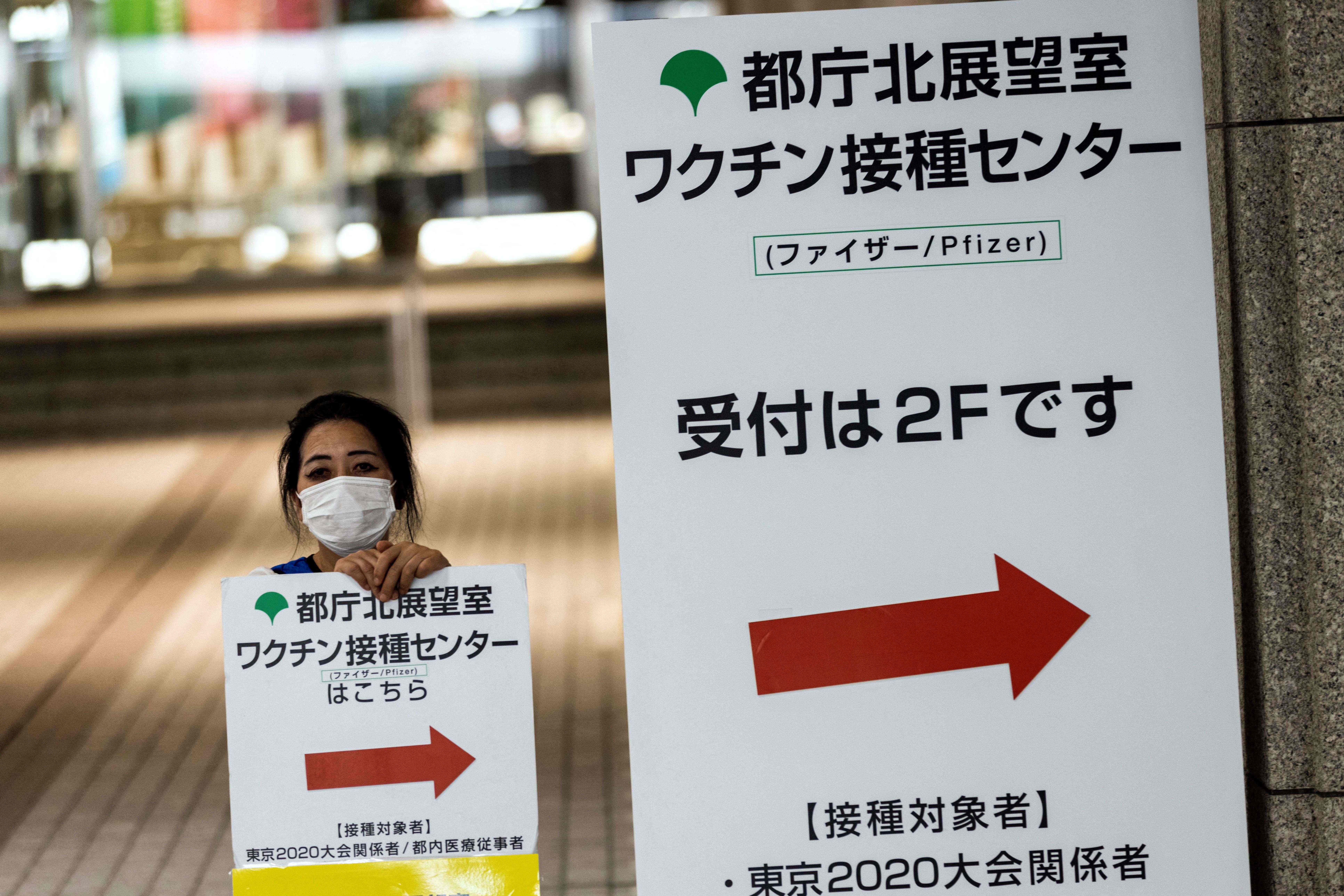 An employee sits next to signboards showing the location of a Pfizer Covid-19 coronavirus vaccination centre at the Tokyo Metropolitan Government building in Tokyo on July 15, 2021.