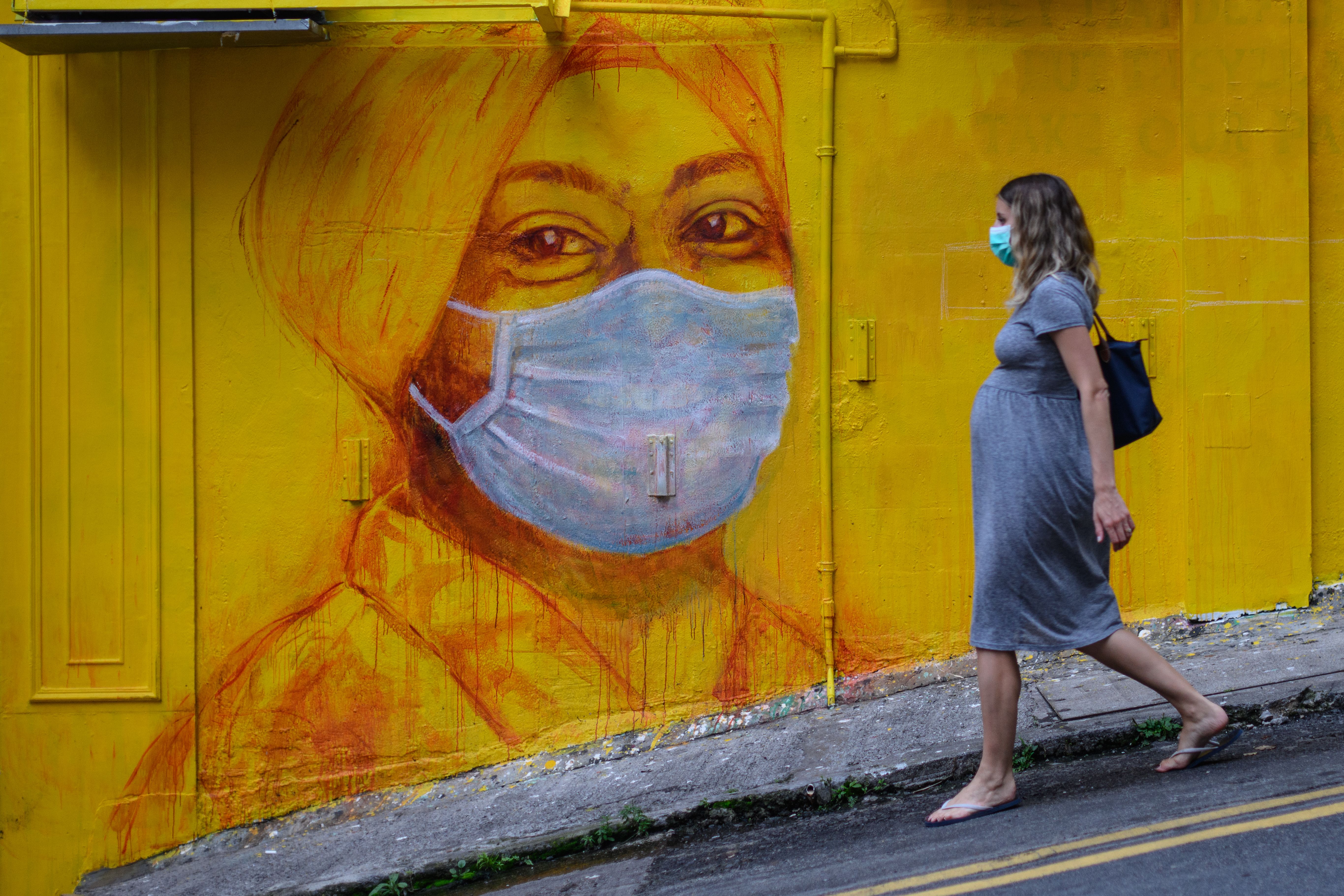 A pregnant woman wearing a face mask as a precautionary measure walks past a street mural in Hong Kong, on March 23, 2020