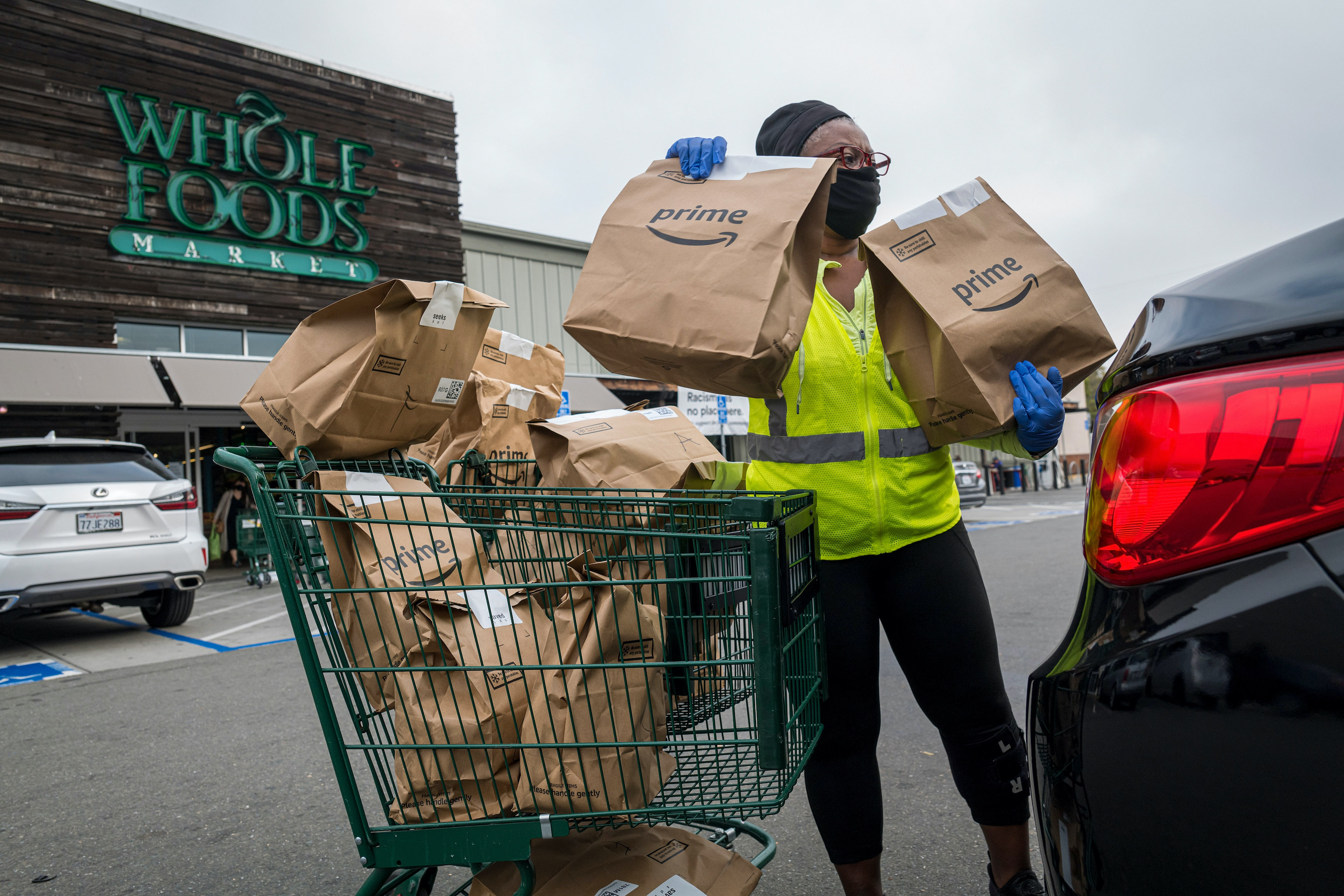 An independent contractor wearing a protective mask and gloves loads Amazon Prime grocery bags into a car outside a Whole Foods Market in Berkeley, California, on October 7, 2020.