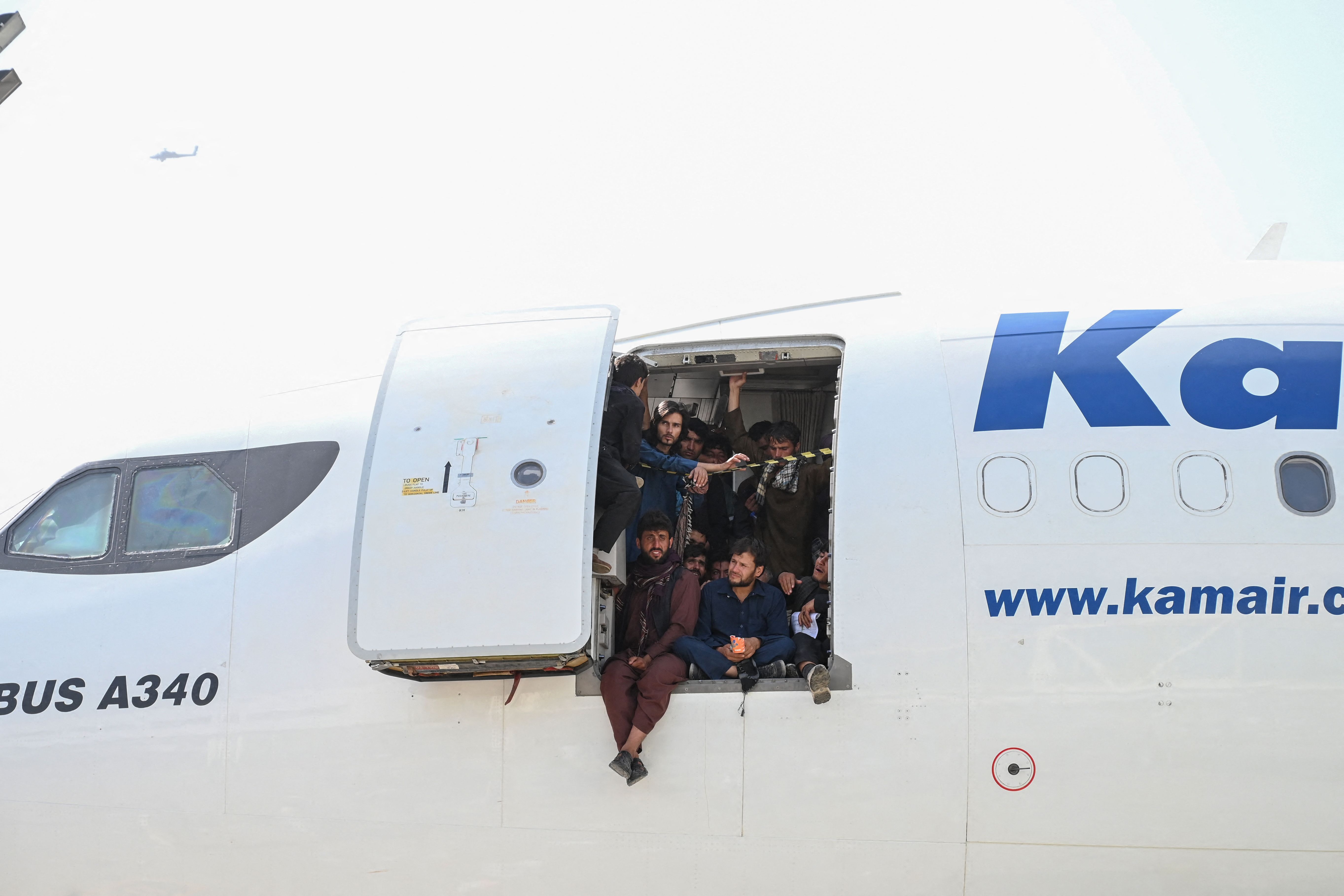 Afghan people climb up on a plane and sit by the door as they wait at the Kabul airport on August 16, 2021. Thousands of people mobbed the city's airport trying to flee the Taliban's feared hardline brand of Islamist rule.