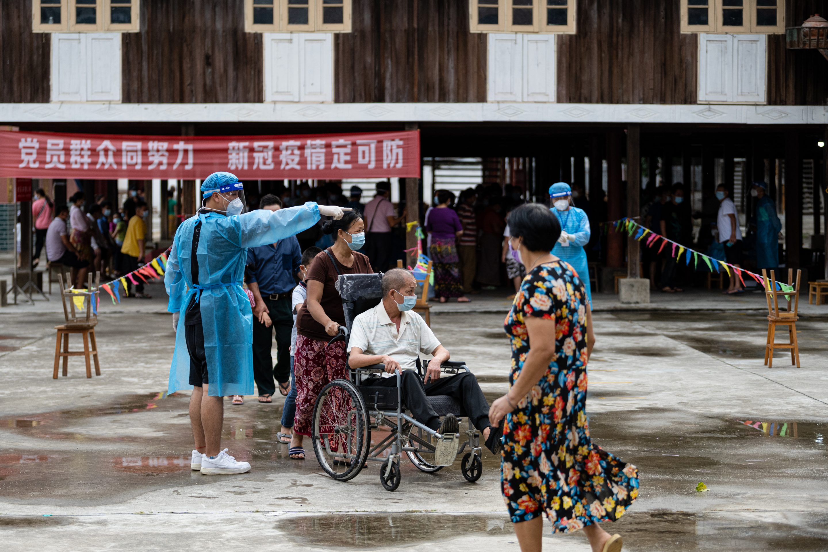 A woman pushes her family member in a wheelchair at a nucleic acid testing site on August 7, 2021 in Ruili, Yunnan Province of China.