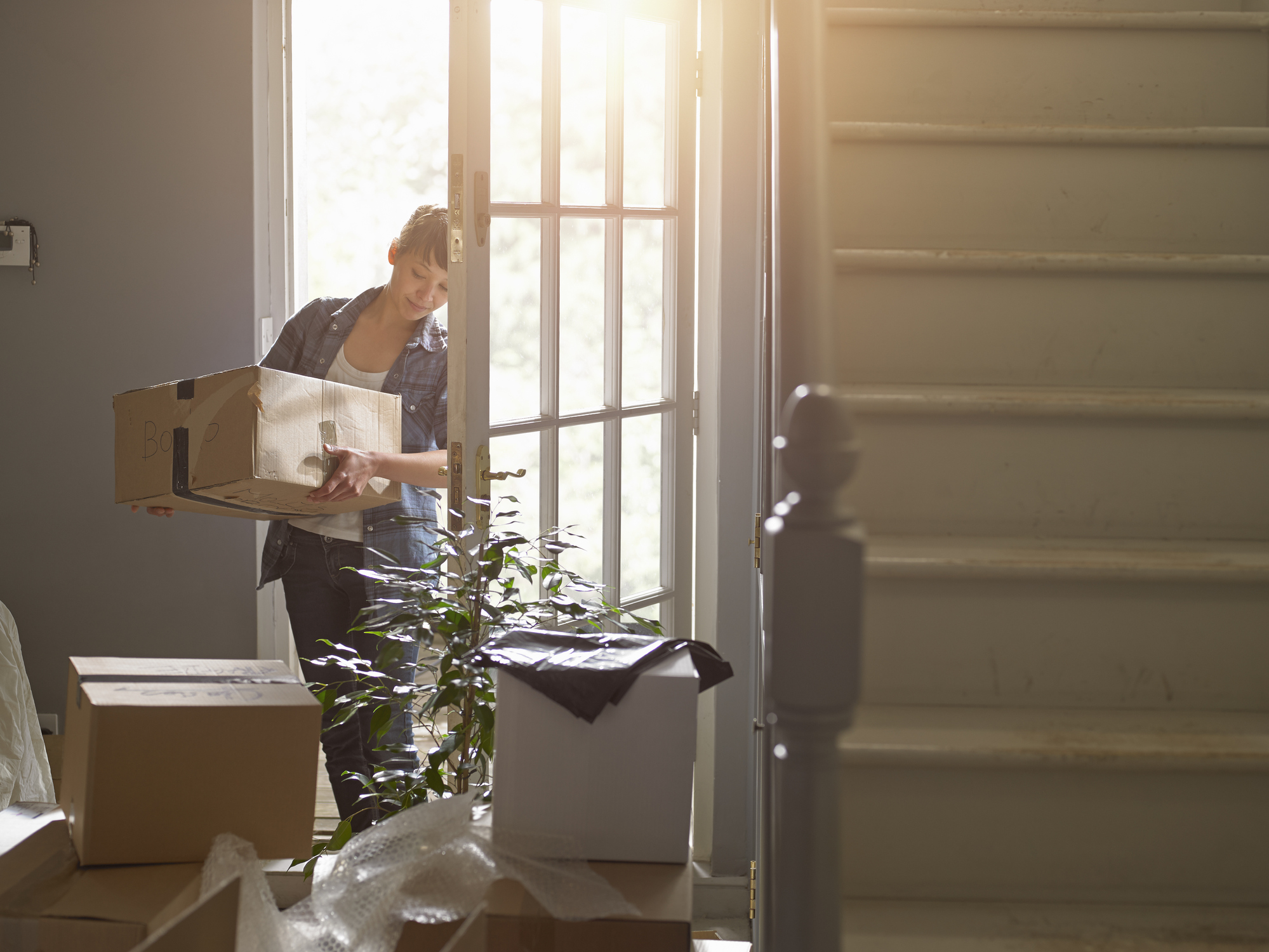 A woman carrying a packing box into her new home.