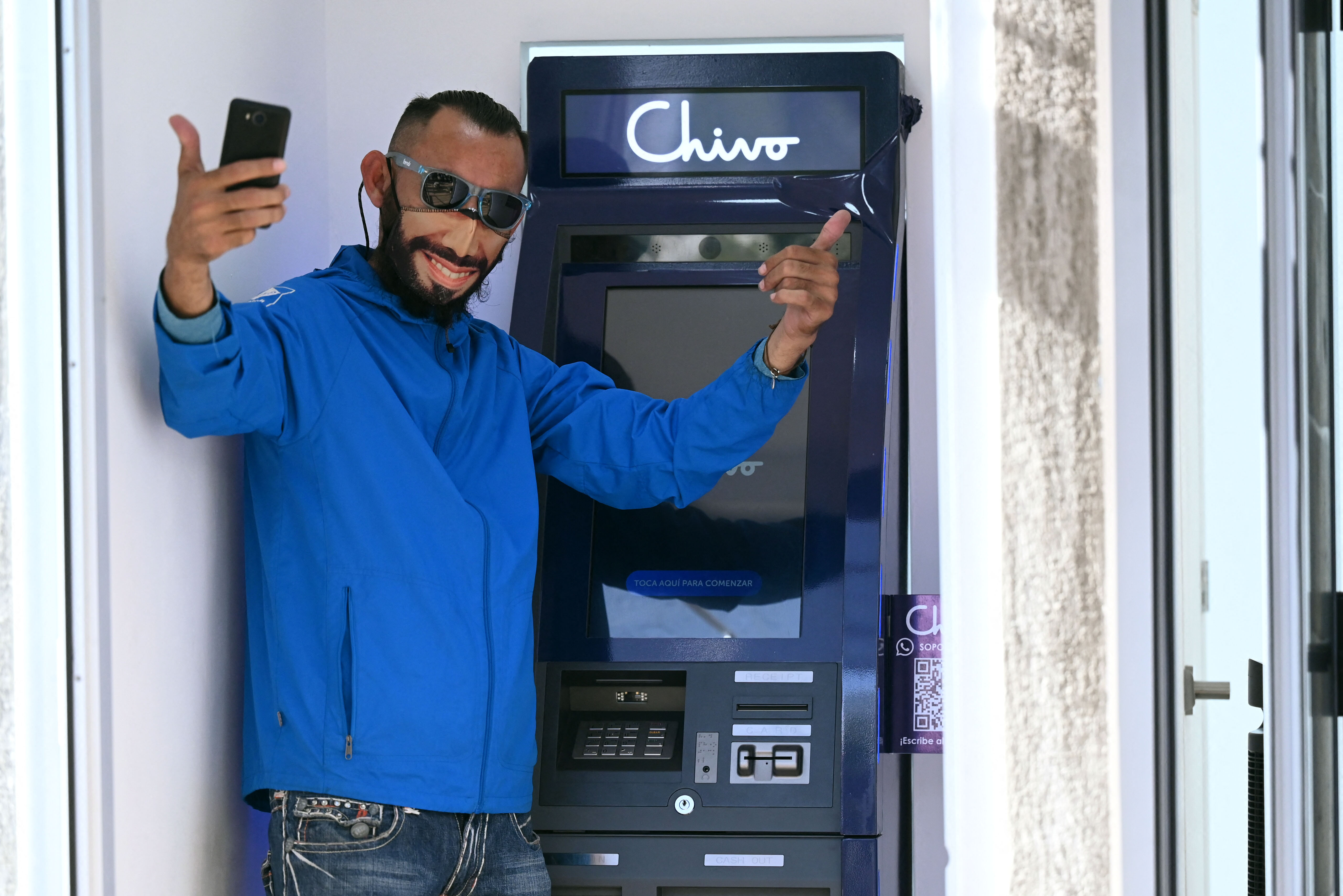 A man wearing a protective face mask with the image of Salvadoran President Nayib Bukele poses for a picture at a Bitcoin ATM in San Salvador on Sept. 7, 2021.