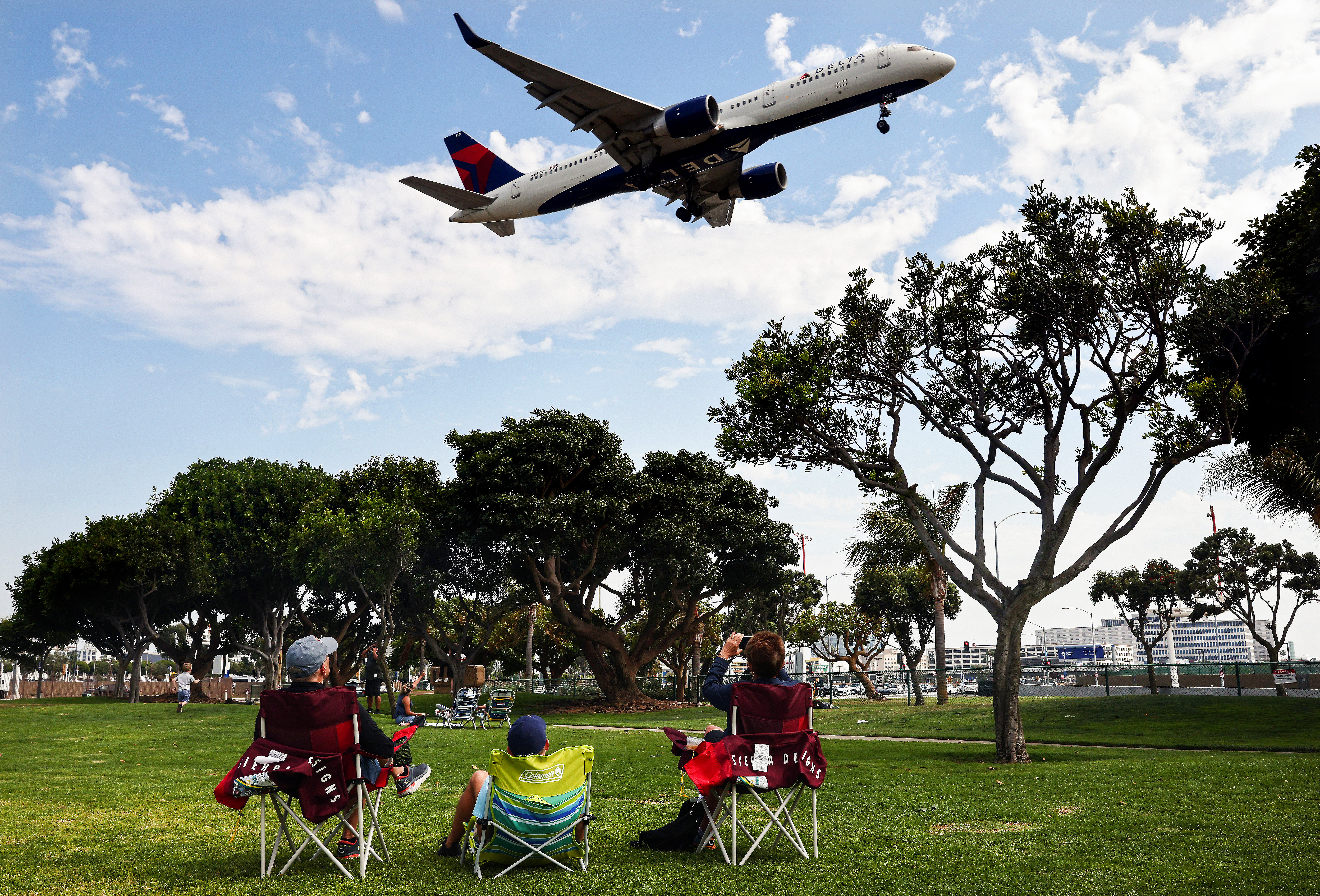 People in a park near Los Angeles International Airport watch a Delta Air Lines plane land on Aug. 25, 2021. Delta is increasing health insurance premiums for unvaccinated employees by $200 a month to cover higher costs of COVID-related care.