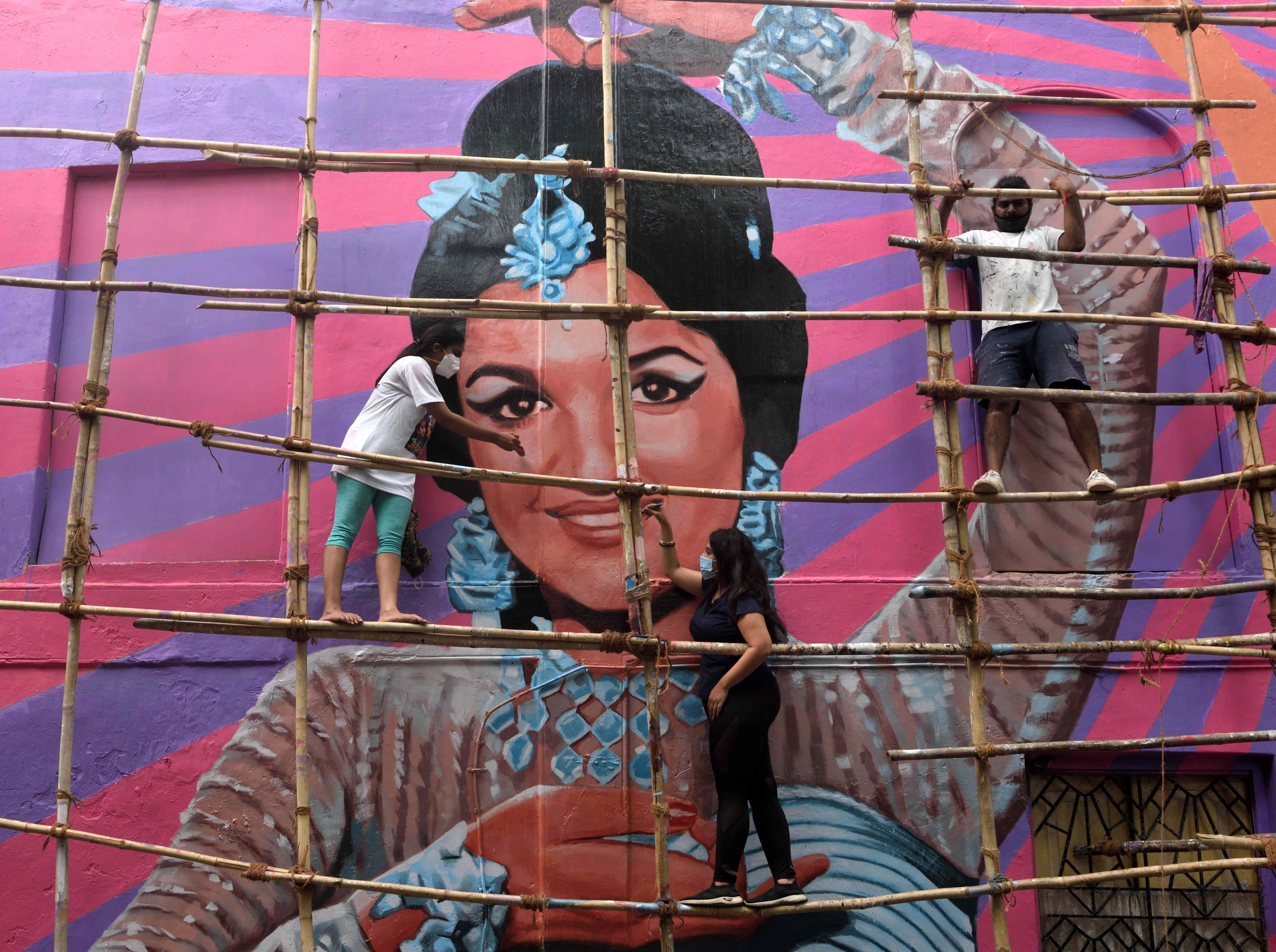 An artist wearing a facemask as a preventive measure against the spread of the Covid-19 coronavirus paints a wall mural of Bollywood actress Asha Parekh on a residential building at Bandra, on May 16, 2021 in Mumbai, India.