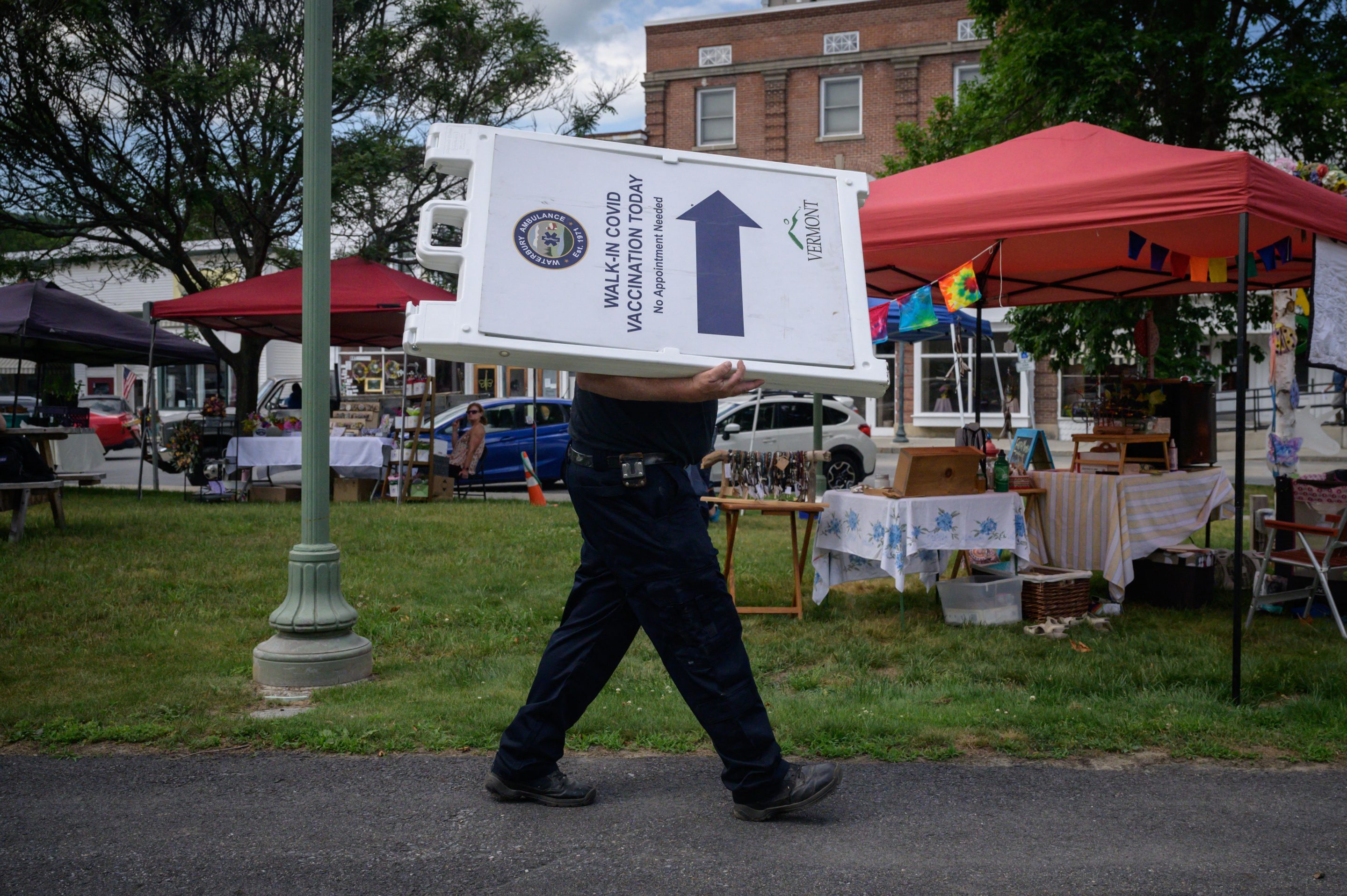 An EMT worker carries a sign advertising free vaccinations against Covid-19 at a farmers market in Northfield, Vermont on June 28, 2021. Despite having the country's highest vaccination rate, Vermont has experienced the biggest surge of COVID cases over the past two weeks as cases drop across the U.S. (Photo by Ed JONES / AFP)