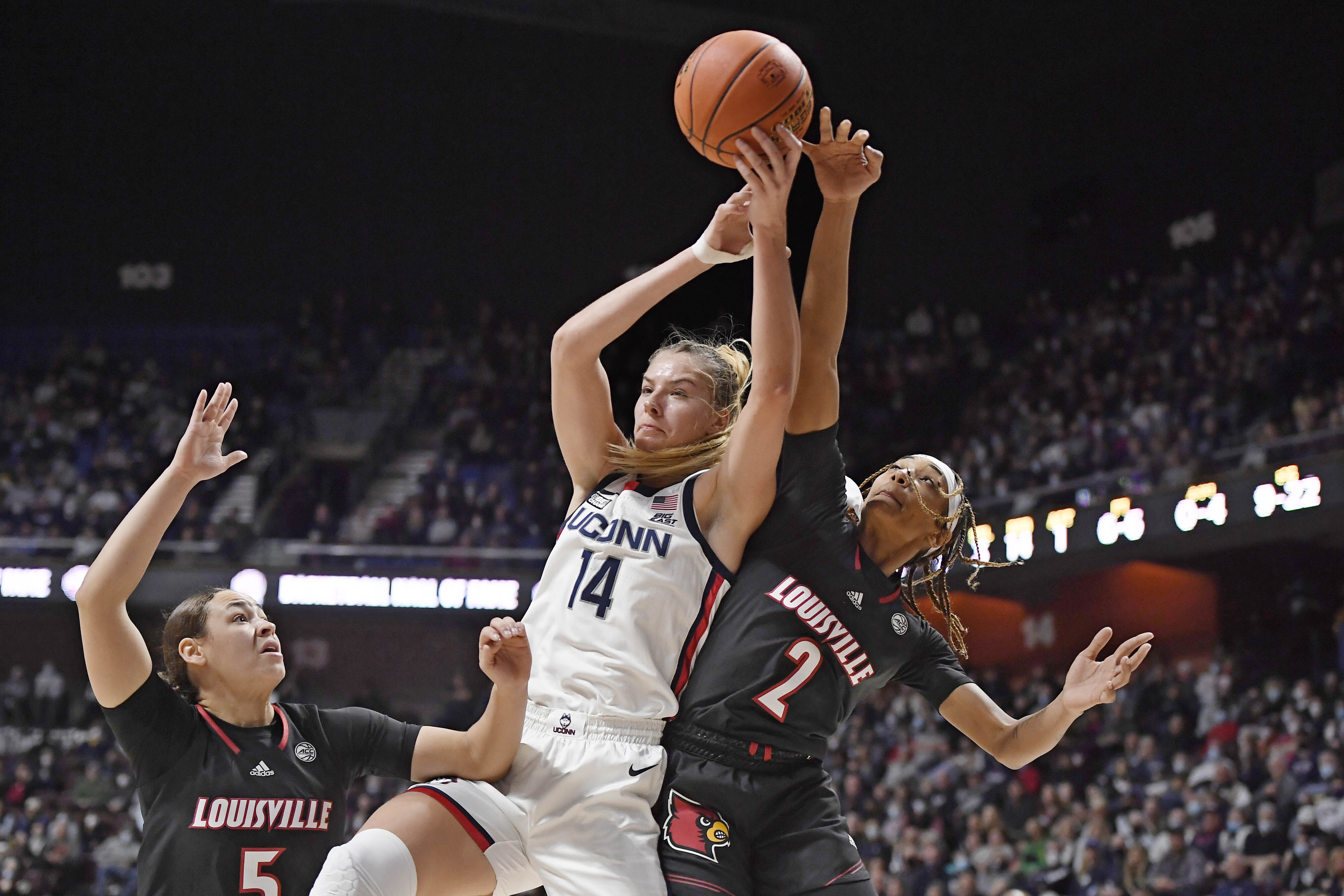 Connecticut's Dorka Juhasz (14) reaches up for a rebound against Louisville's Ahlana Smith (2) as Louisville's Mykasa Robinson (5) defends in the first half of an NCAA college basketball game, Sunday, Dec. 19, 2021, in Uncasville, Conn.