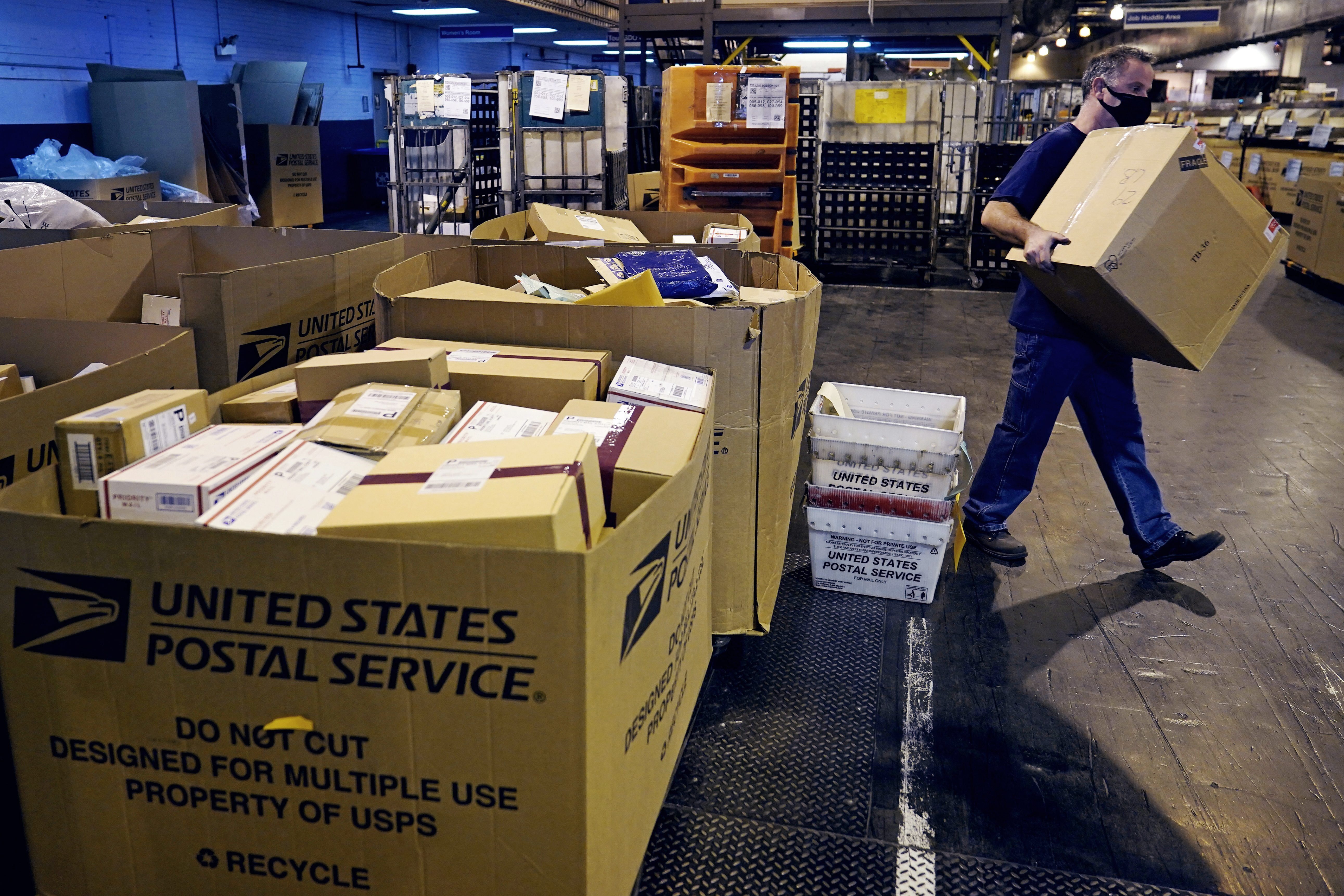 A worker carries a large parcel at the United States Postal Service sorting and processing facility, Thursday, Nov. 18, 2021, in Boston. The U.S Postal Service pulled out all the stops to avoid a repeat of the 2020 holiday shipping disaster, and it worked. The Postal Service and several other private shippers reported that holiday season deliveries went smoothly, for the most part.