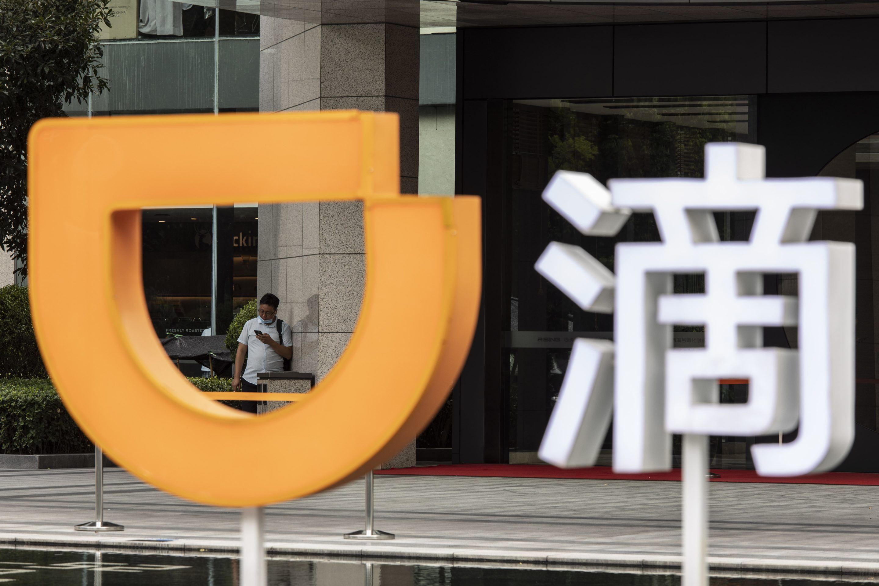A pedestrian stands behind a logo at the Didi Global Inc. offices in Hangzhou, China, on Aug. 2, 2021. 