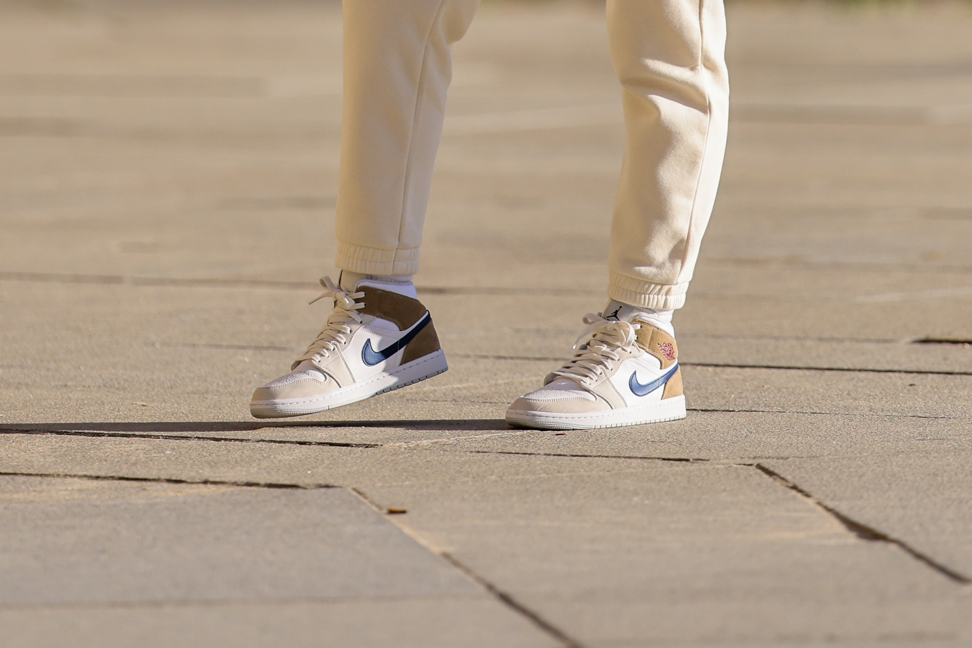 A passerby wears high waist white latte jogging / sport pants, white socks, white leather / brown suede with black leather logo ankle sneakers from Nike, on November 29, 2021 in Paris, France.