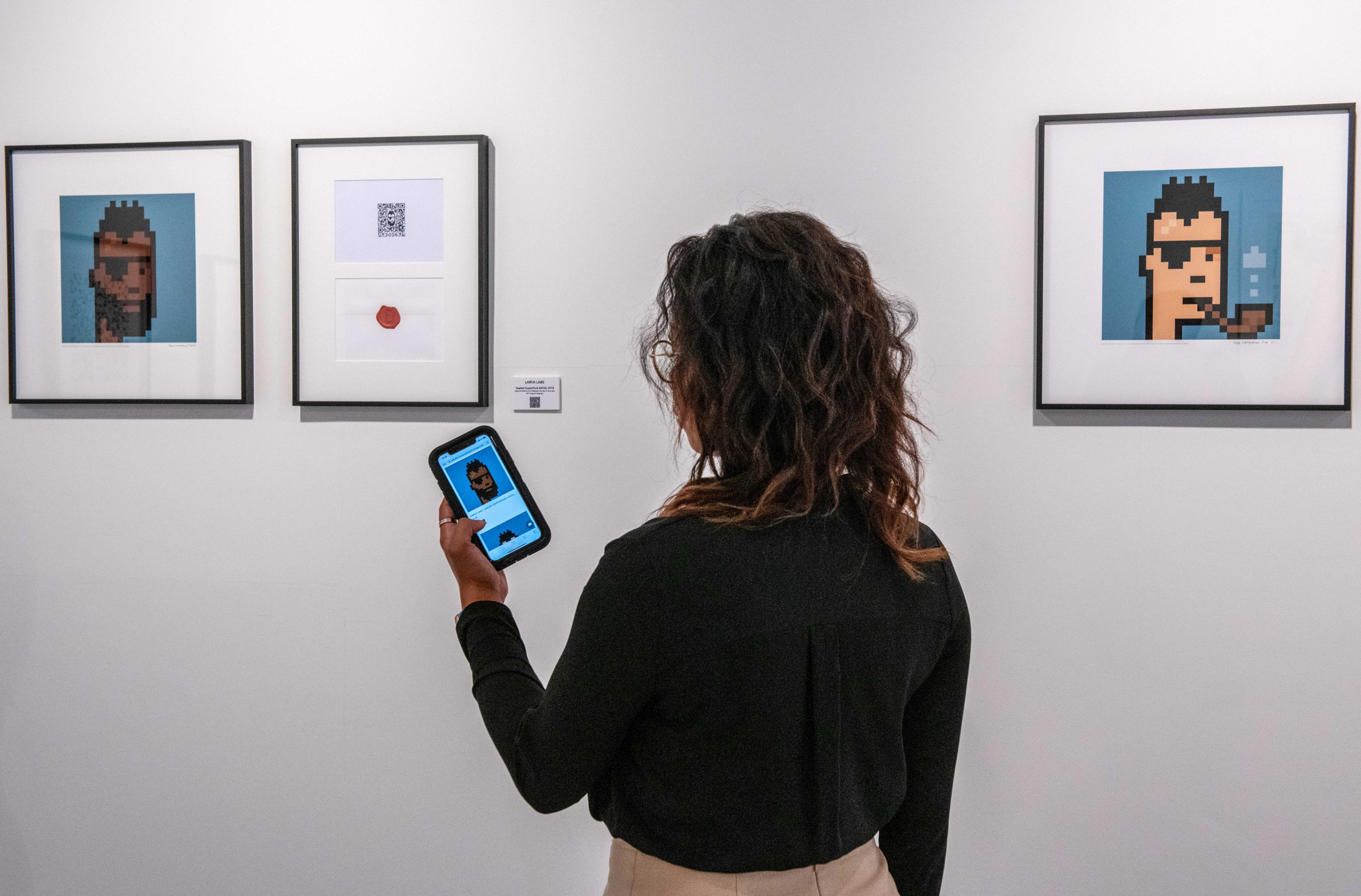 A gallery assistant holds up a smartphone displaying the gallery’s online marketplace near an NFT and signed lithograph “Sealed Cryptopunk #3036,” by Larva Labs, during the press preview of the “Portrait of an Era” exhibition, at the House of Fine Art (HOFA) in London, on Sept. 22, 2021. A report by DappRadar said NFTs have held their value better since November than the two most popular cryptocurrencies, Bitcoin and Ether.