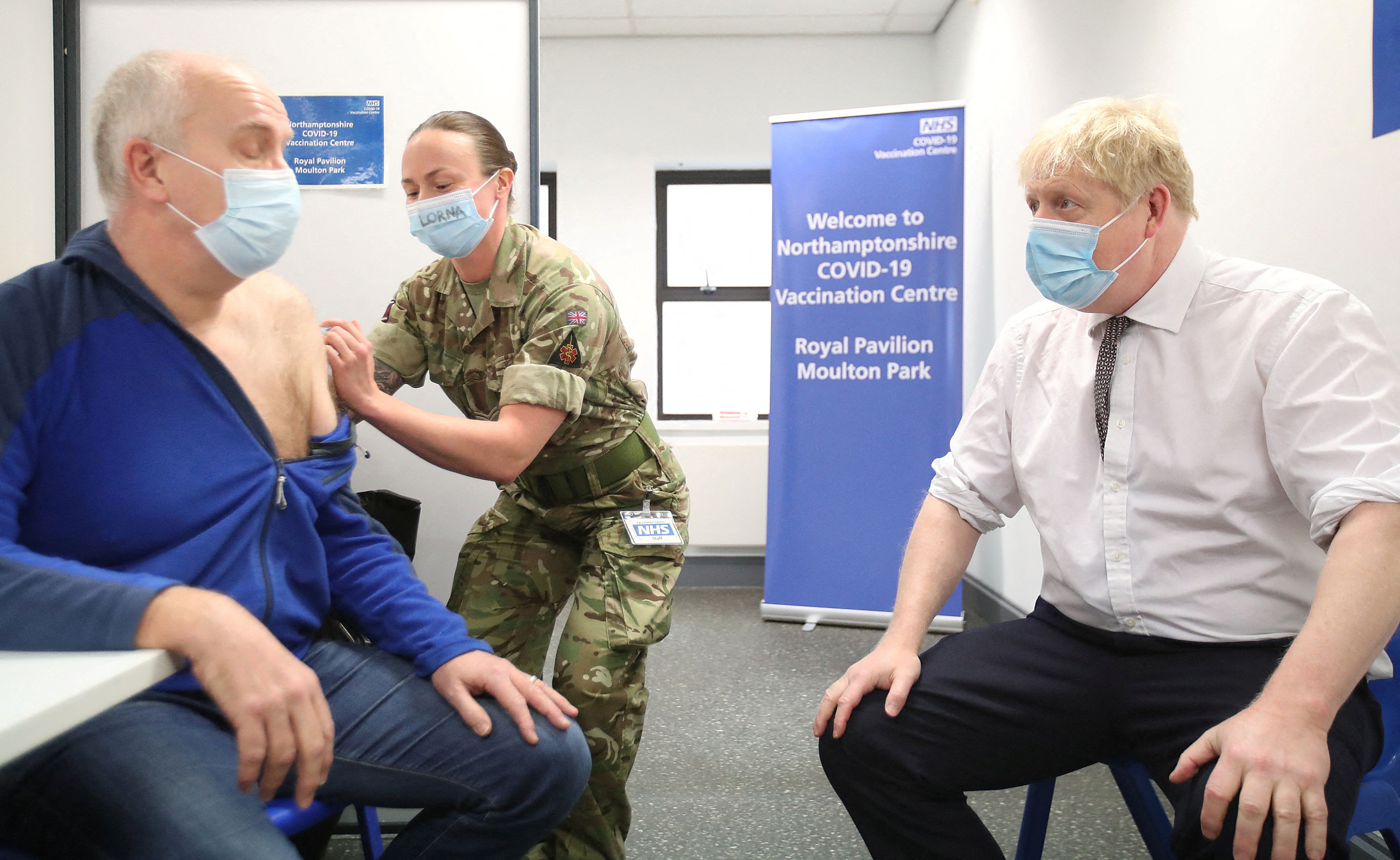 Britain's Prime Minister Boris Johnson (R) sits opposite Gordon Halfacre as he receives his Covid-19 vaccine from corporal Lorna MacDonald during a visit to a vaccination centre in Northampton on January 6, 2022. - The UK government announced changes to Covid travel rules for England, scrapping the need for visitors to have pre-departure tests and quarantine on arrival until they have tested negative. (Photo by PETER CZIBORRA / POOL / AFP) (Photo by PETER CZIBORRA/POOL/AFP via Getty Images)