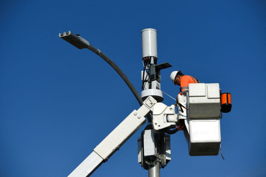 A contractor installs 5G cellular equipment on a light pole.