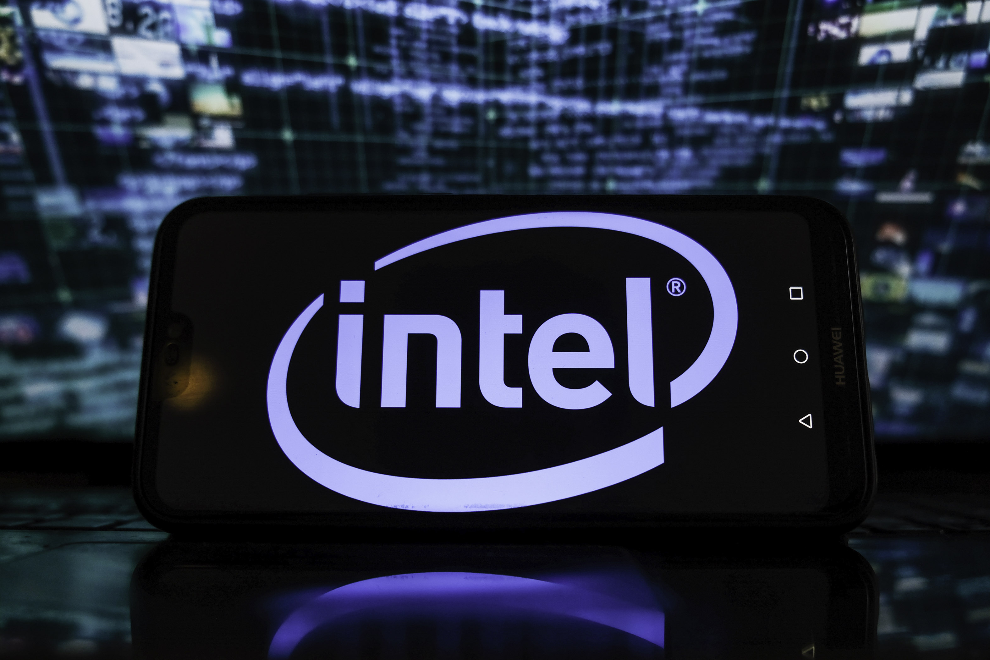 In this photo illustration, an Intel logo is displayed on a smartphone with stock market graphics in the background.