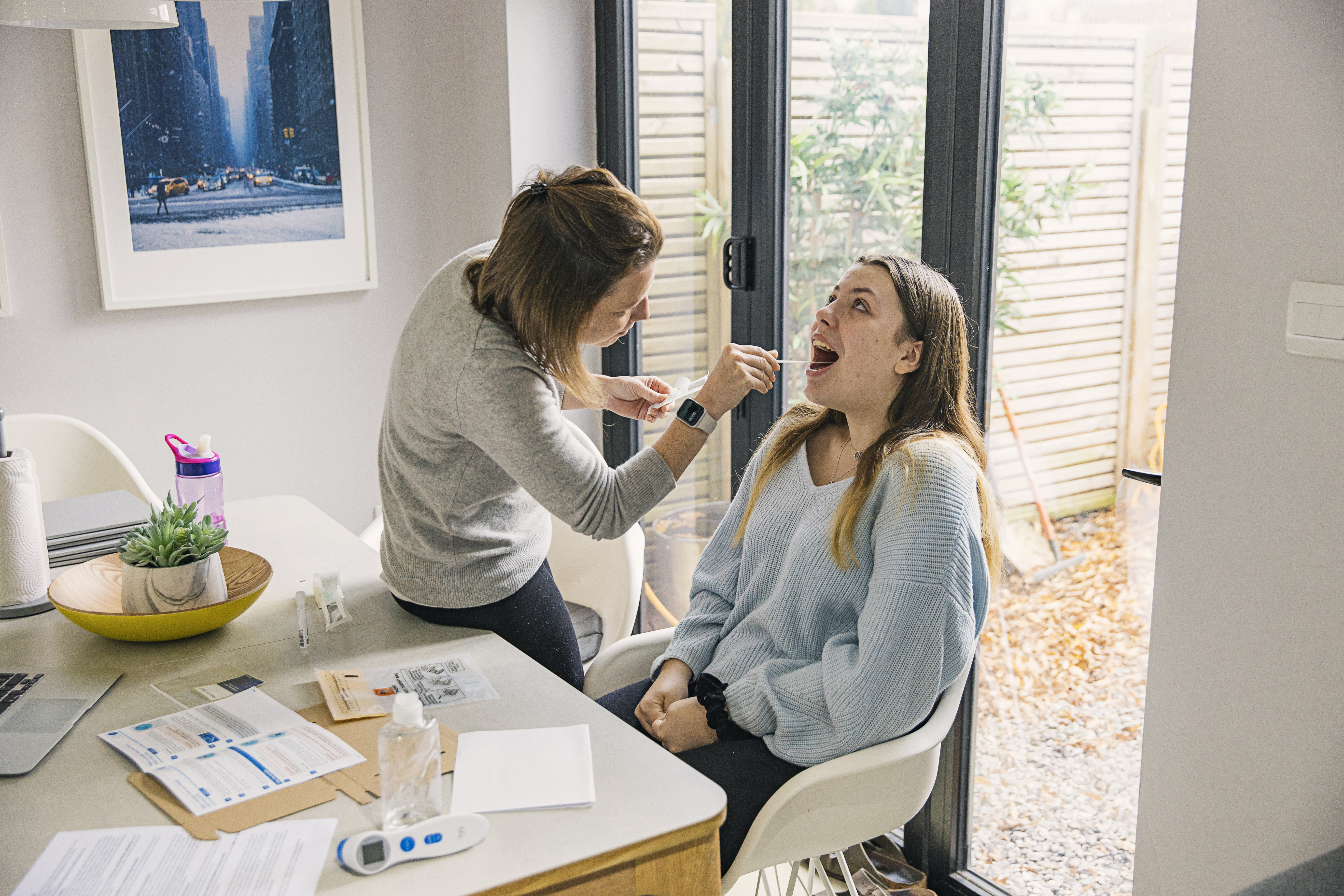Woman using home COVID-19 testing kit on her teenage daughter.