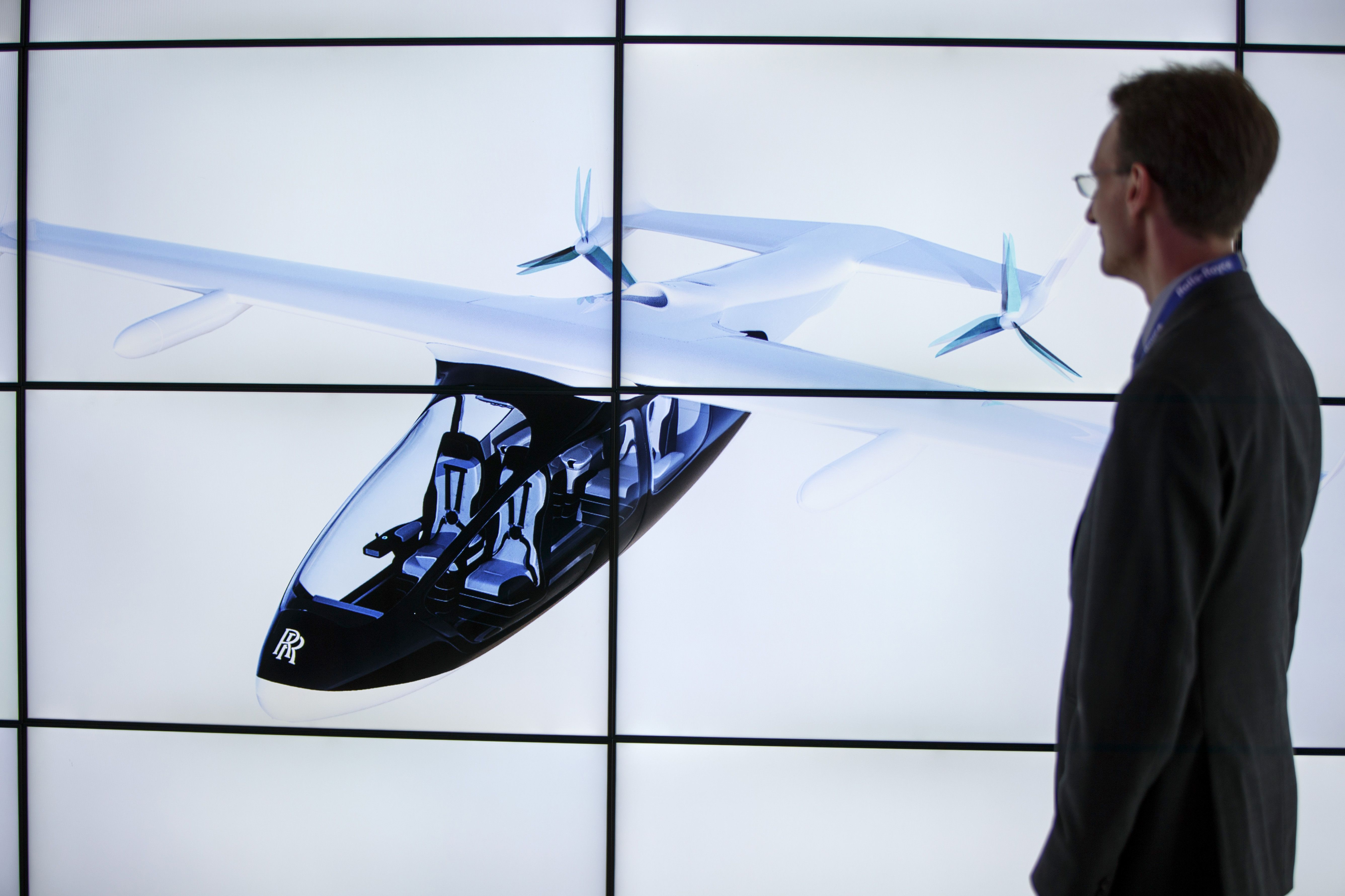 A man poses alongside screens presenting the Rolls-Royce EVTOL air taxi concept during the Farnborough Airshow, south west of London, on July 16, 2018.