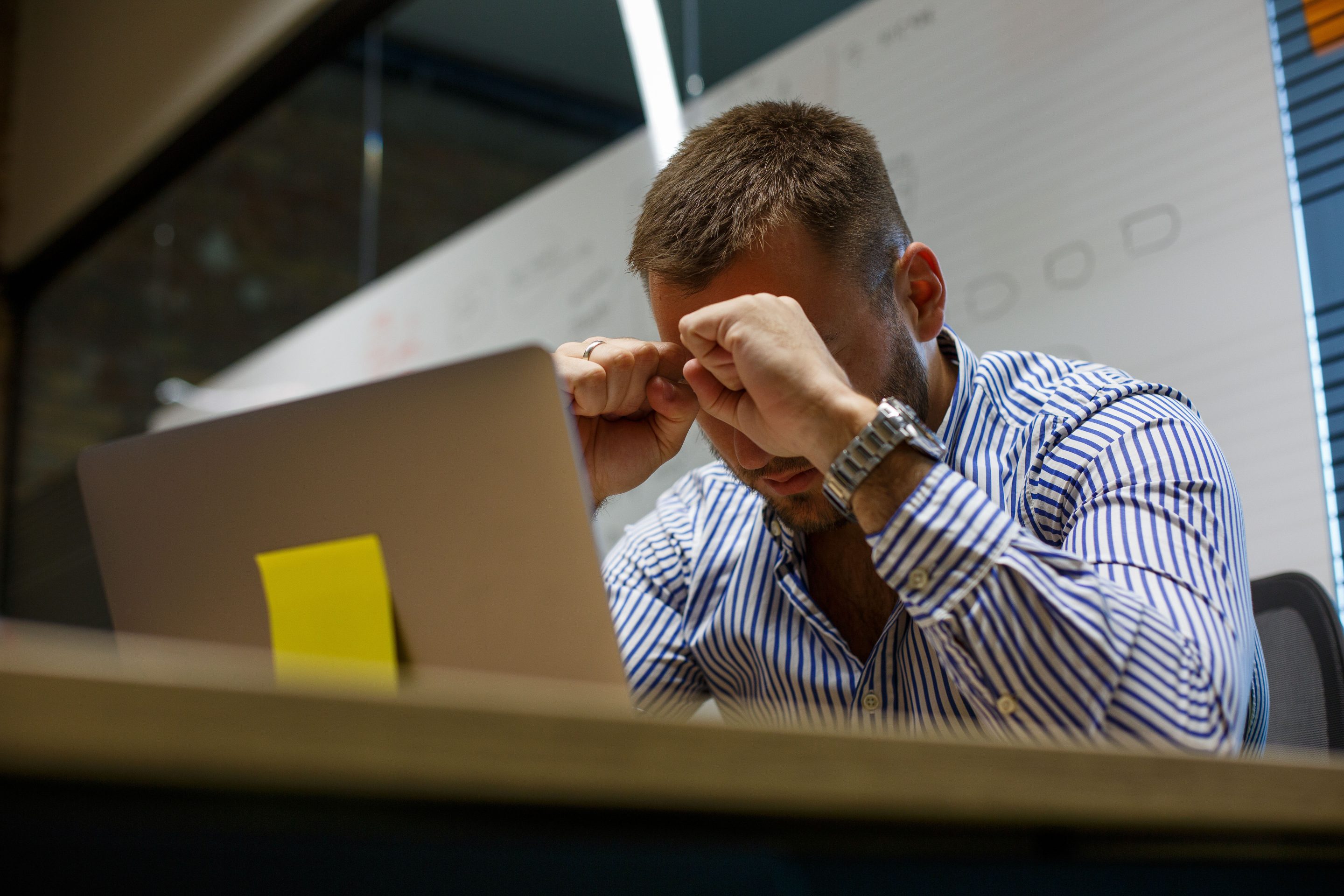 Young man sitting rubbing his eyes in front of laptop and trying to finish his work.