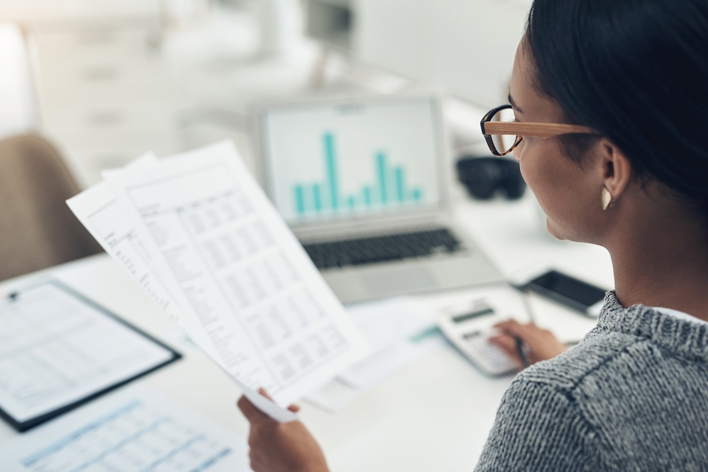 Woman holding papers and using a calculator.