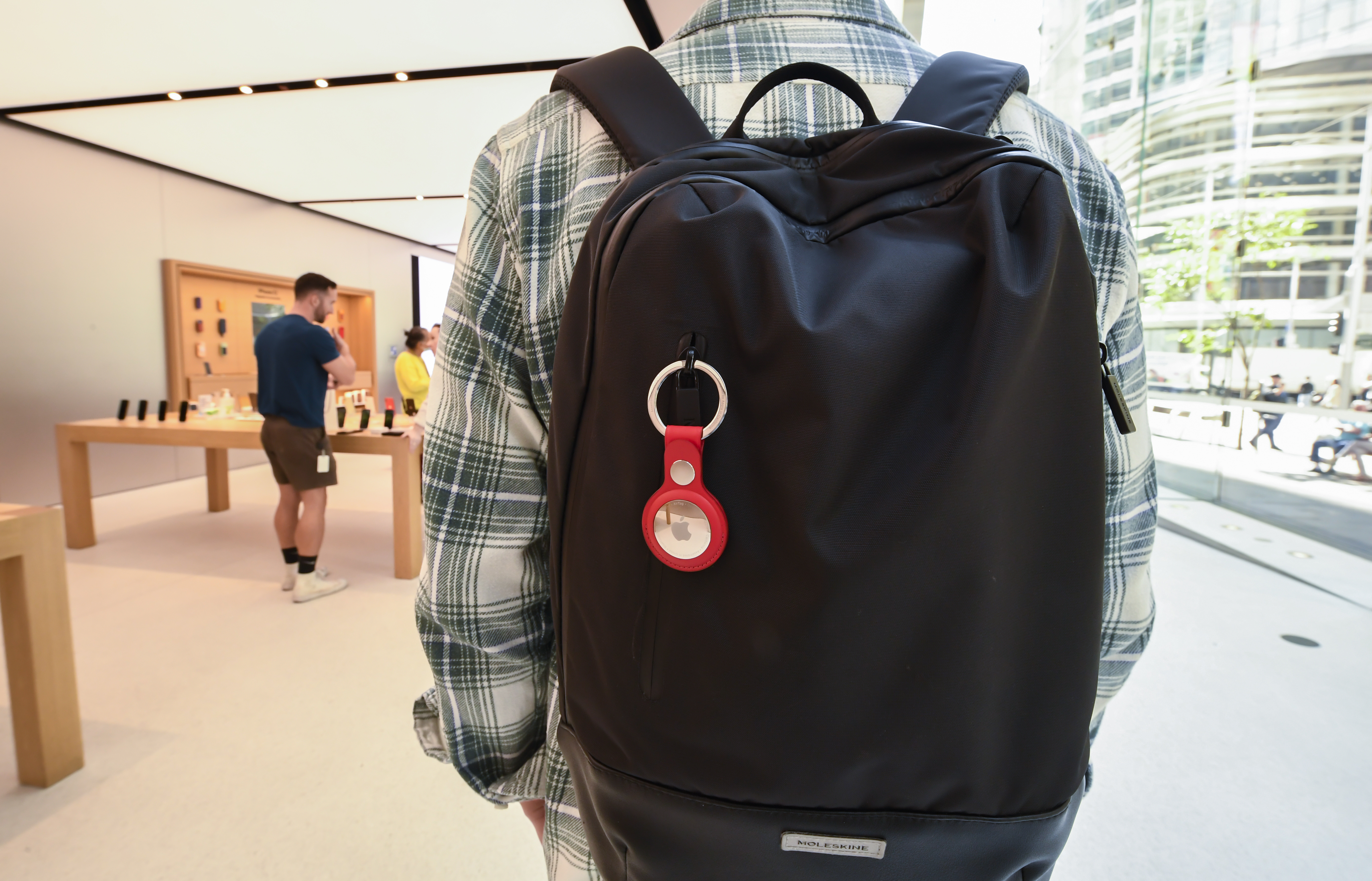 A person wearing a backpack with an attached Apple AirTag and key ring