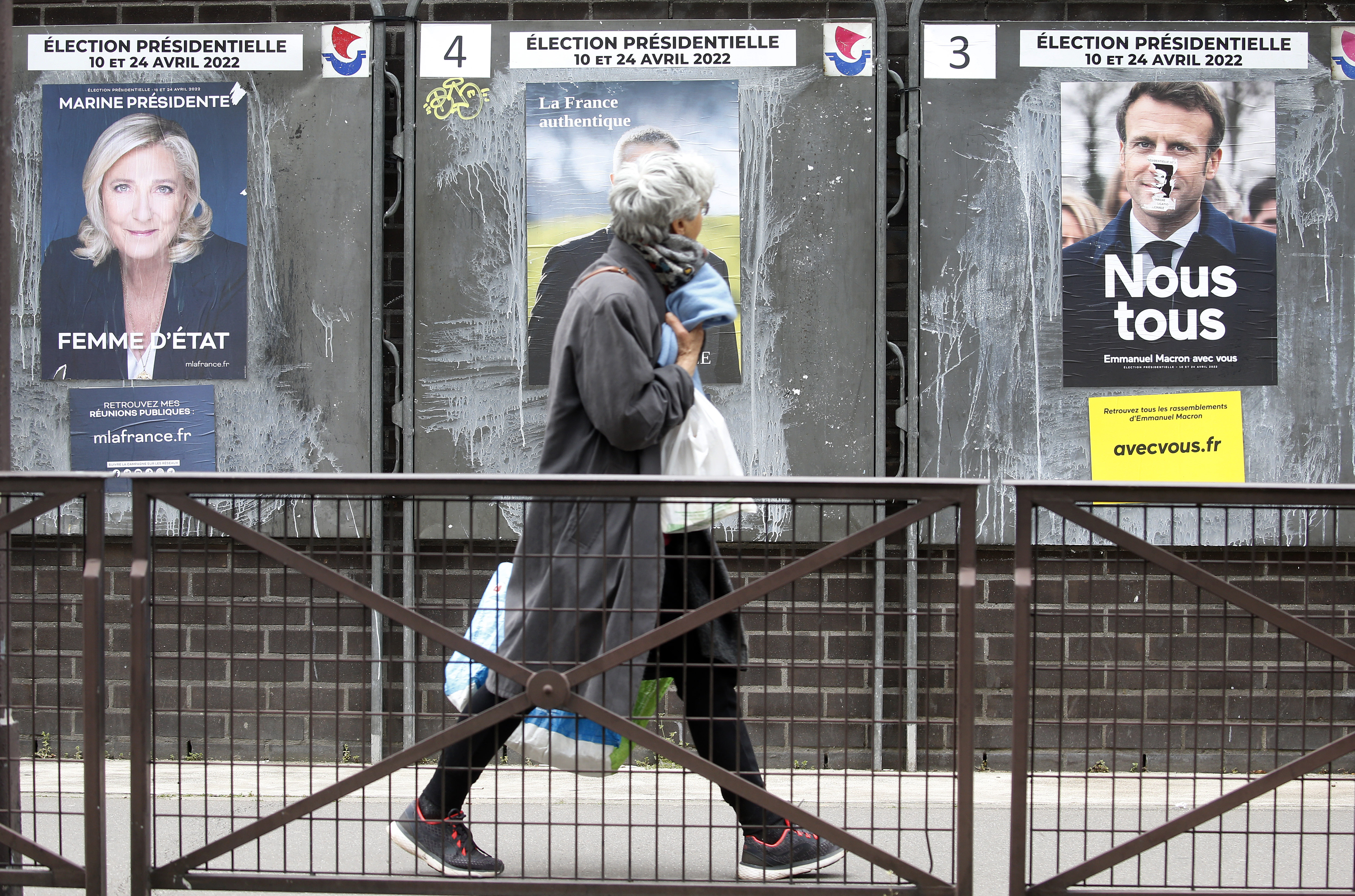 A woman walks past official campaign posters of Marine Le Pen, leader of the far-right Rassemblement national (RN) party and French President Emmanuel Macron 'La République en marche (LREM), candidates in the 2022 French presidential election, displayed on billboards next to a polling station on April 04 in Paris, France.