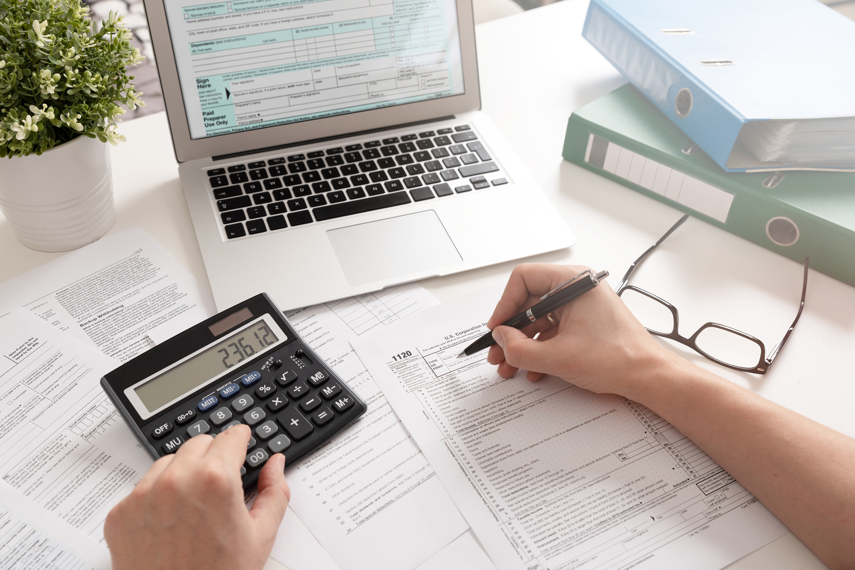 Person writing on tax documents and using a calculator.