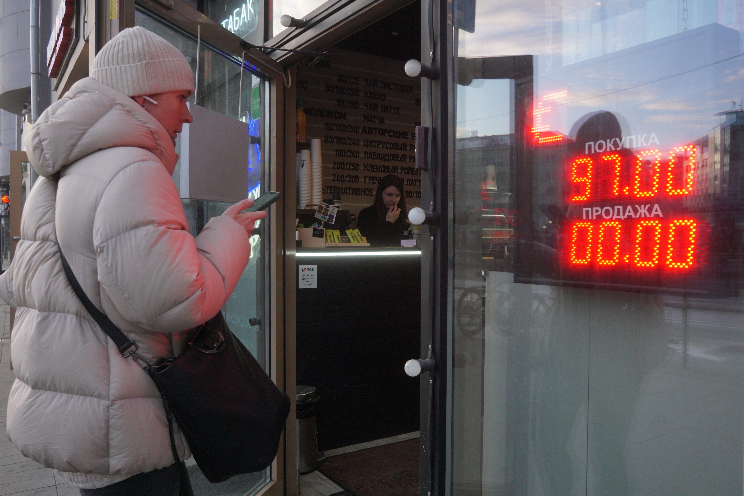A woman walks into a store with the exchange price of the Russian ruble to U.S. dollar listed next to her.