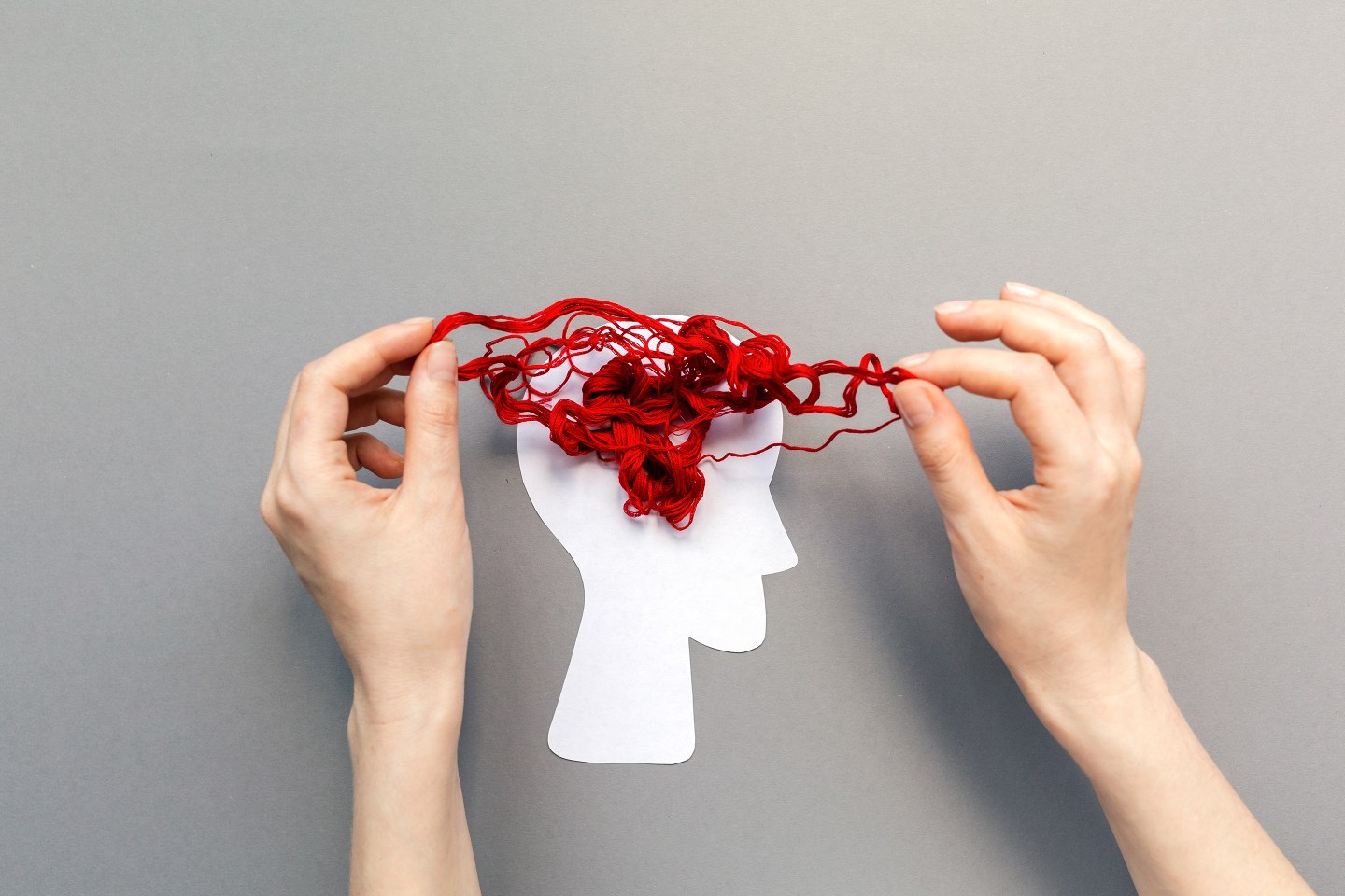 Person untangling thread on top of silhouette of head.