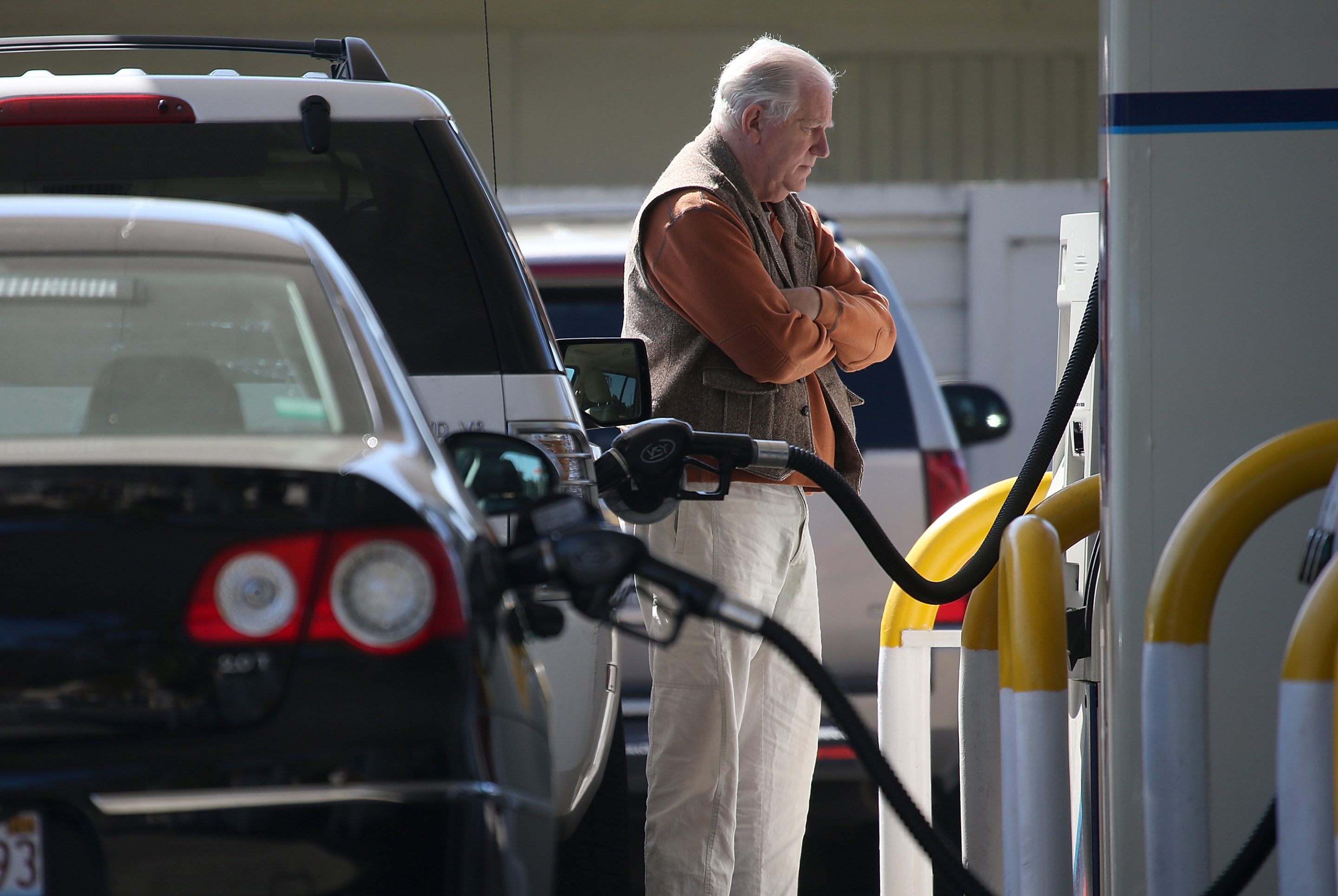 A man stands at a gas pump with arms folded.