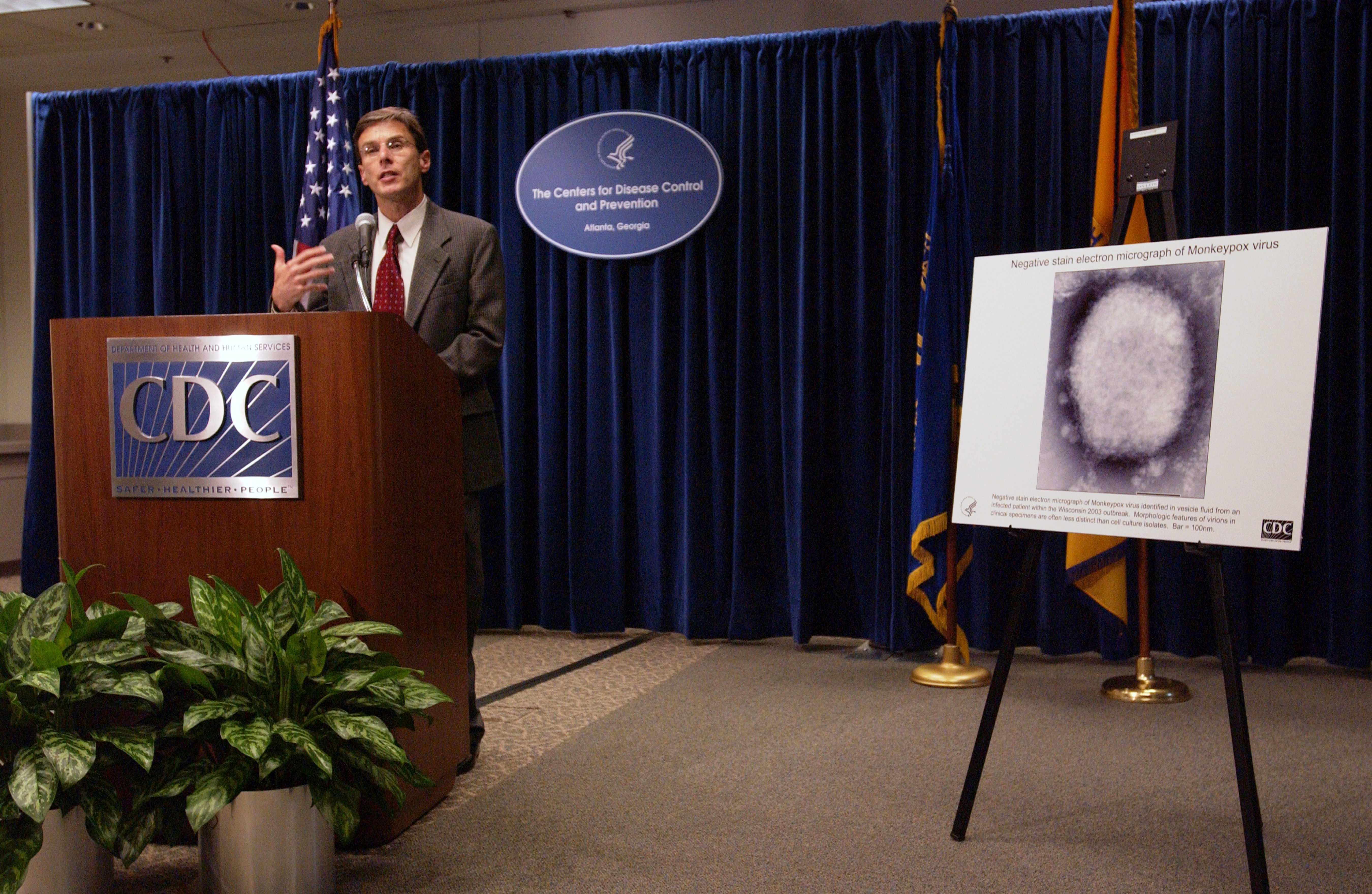 Dr David Fleming addressing the press at a CDC briefing, speaking from a lectern next to a poster as a visual aid in updating the public on the spread of the monkeypox virus and measures taken for its prevention, June 11, 2003. Image courtesy CDC. (Photo by Smith Collection/Gado/Getty Images)
