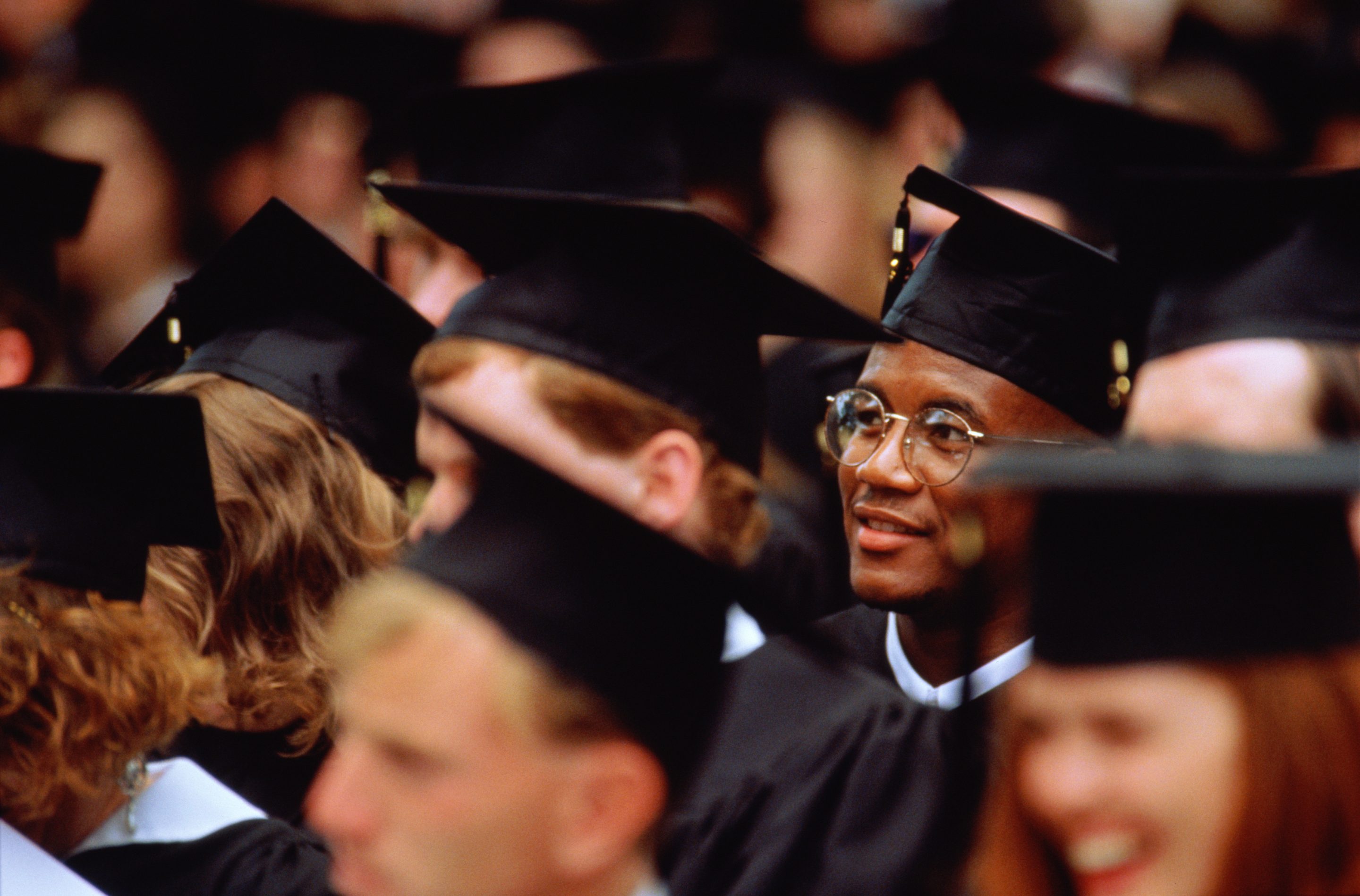 Graduates at graduation ceremony (focus on young man in glasses)
