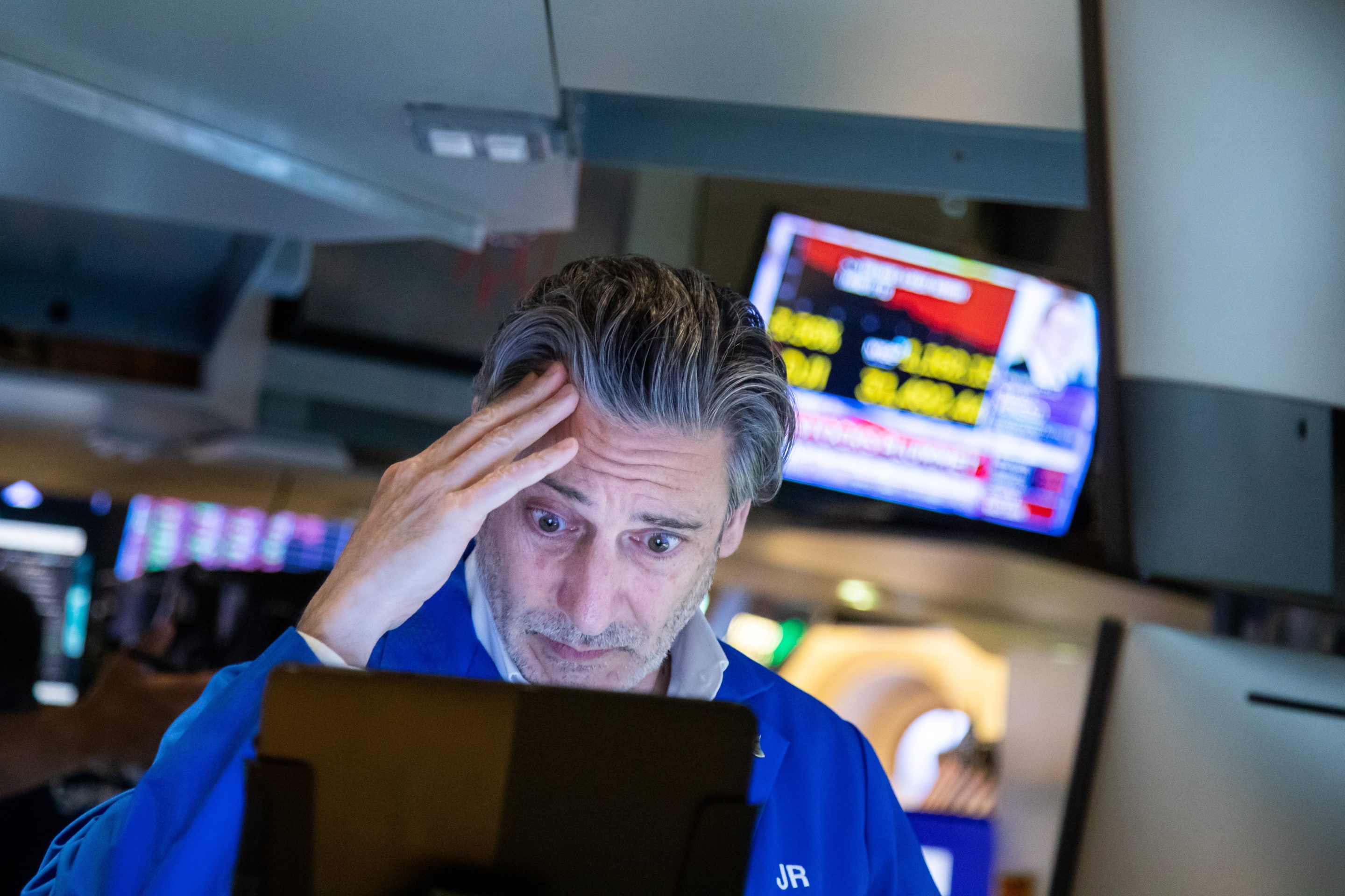 A NYSE trader rubs his head while looking at a computer.