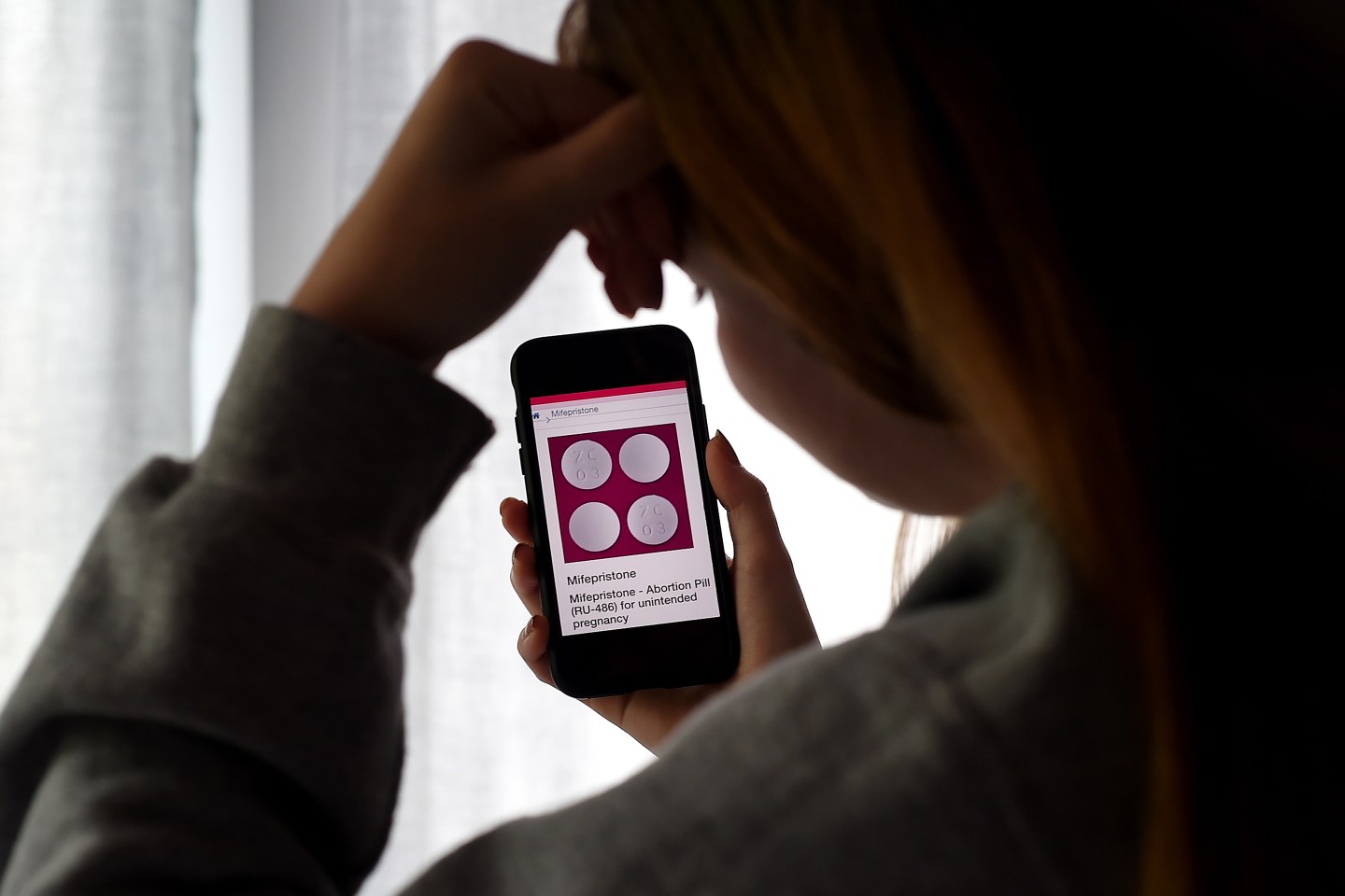 Girl looks at an Abortion Pill (RU-486) for unintended pregnancy from Mifepristone displayed on a smartphone.