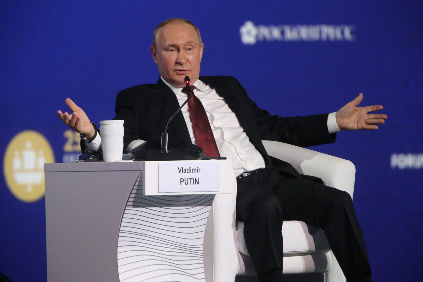 Russia President Vladimir Putin gestures with wide arms while seated on stage at Russia's annual economic forum