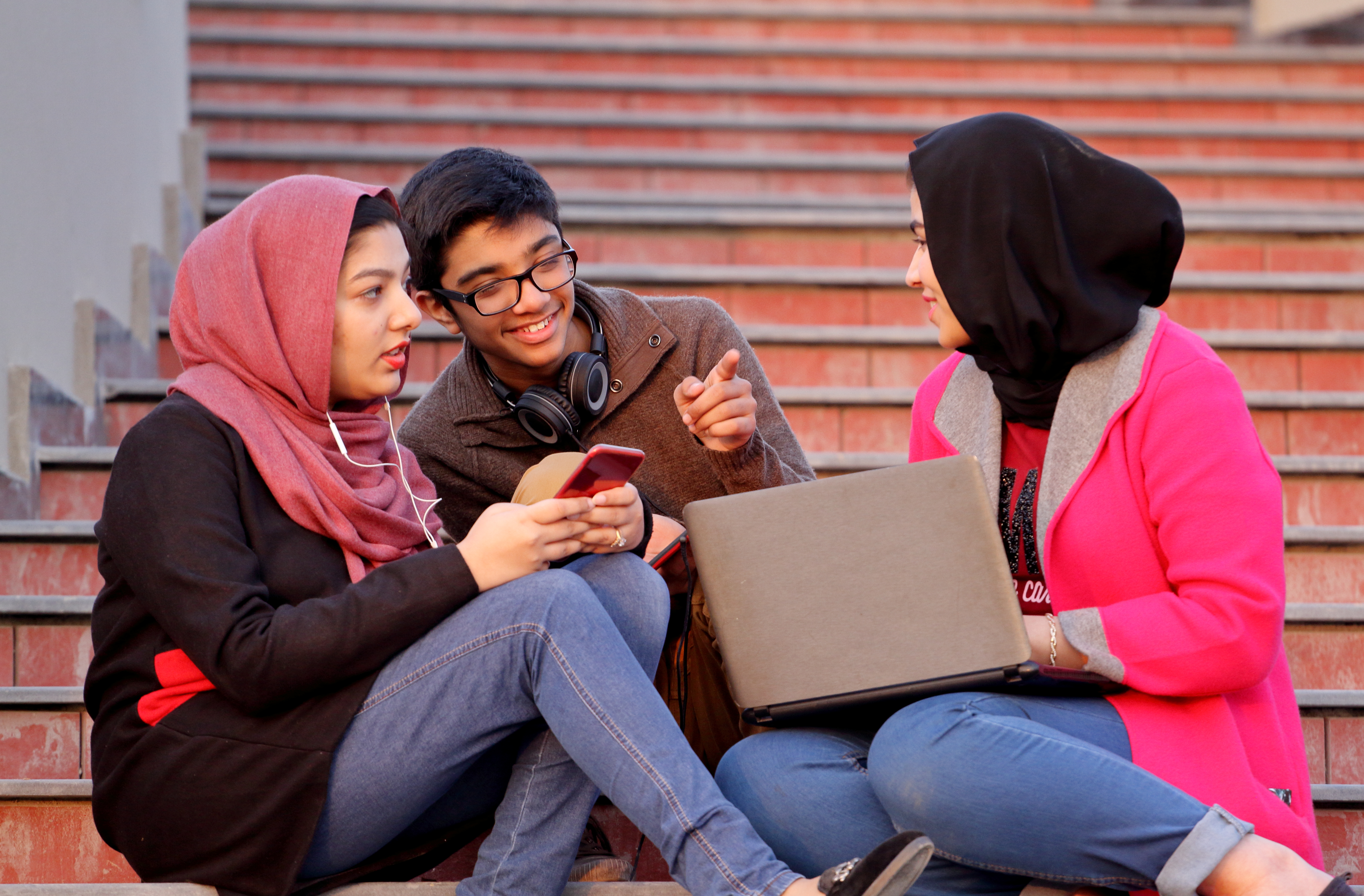 Girls in Hijab (Head Scarf) and a young boy having leisure time together while working on laptop and cell phones.