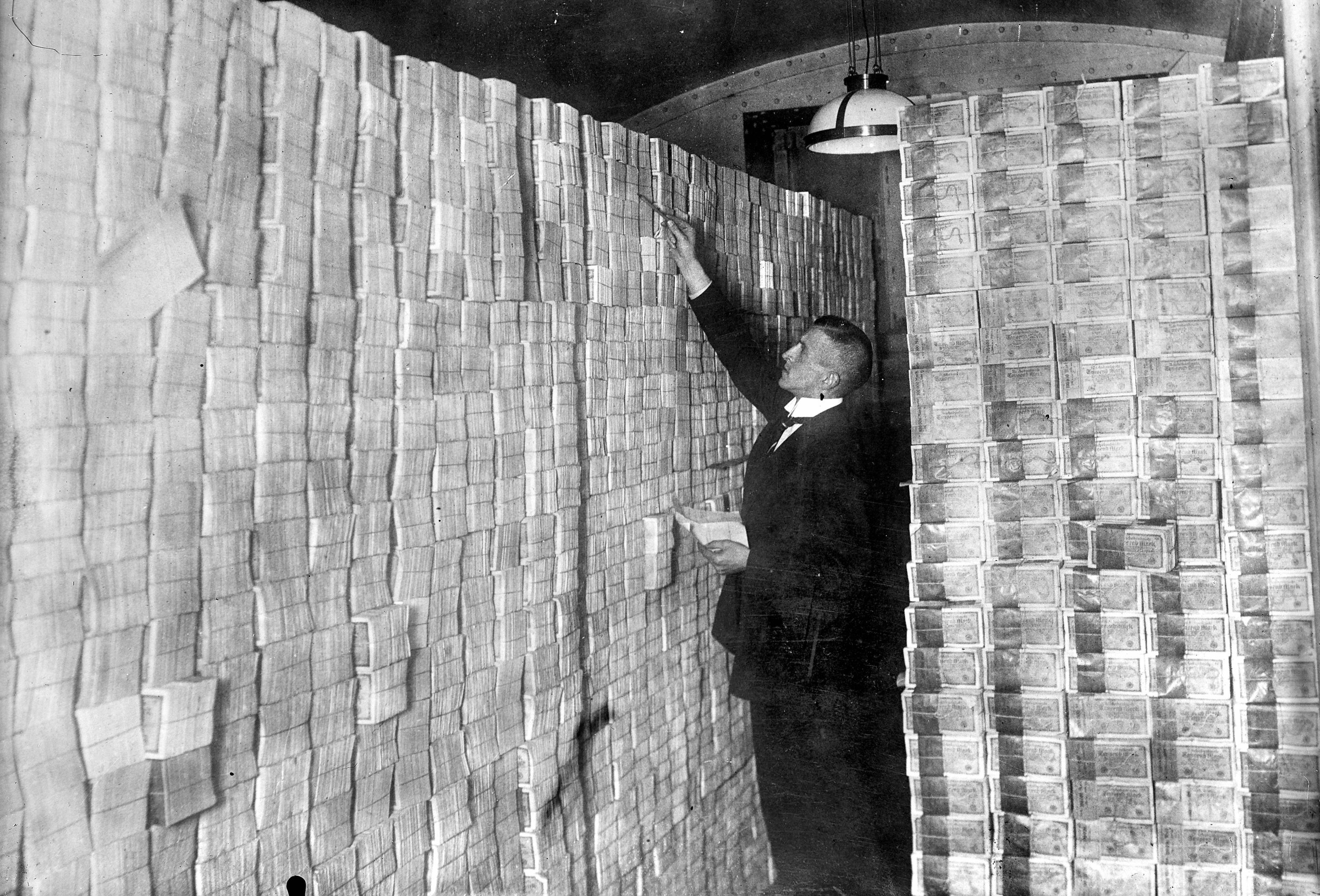 A man stands in front of stacks of banknotes in Germany in 1923.