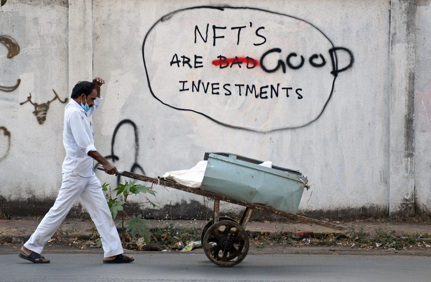 A scrap dealer wearing a protective face mask pushes his handcart past a graffiti painted on a wall that reads "NFT's are good investments" in Mumbai on Feb. 18, 2022.